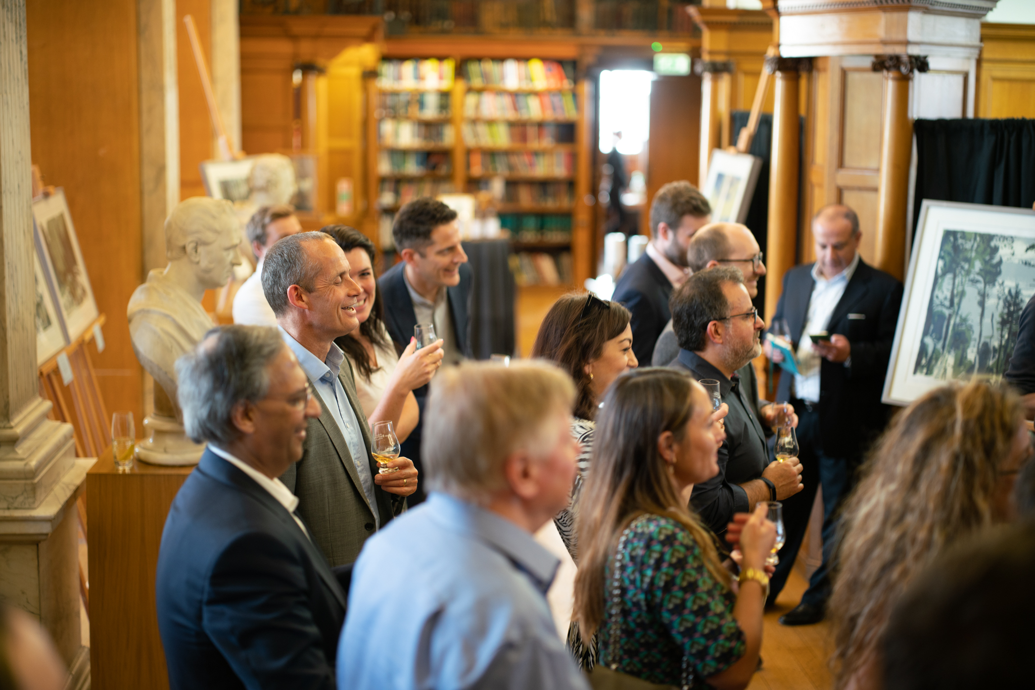 Networking event in elegant library with attendees enjoying refreshments and conversation.