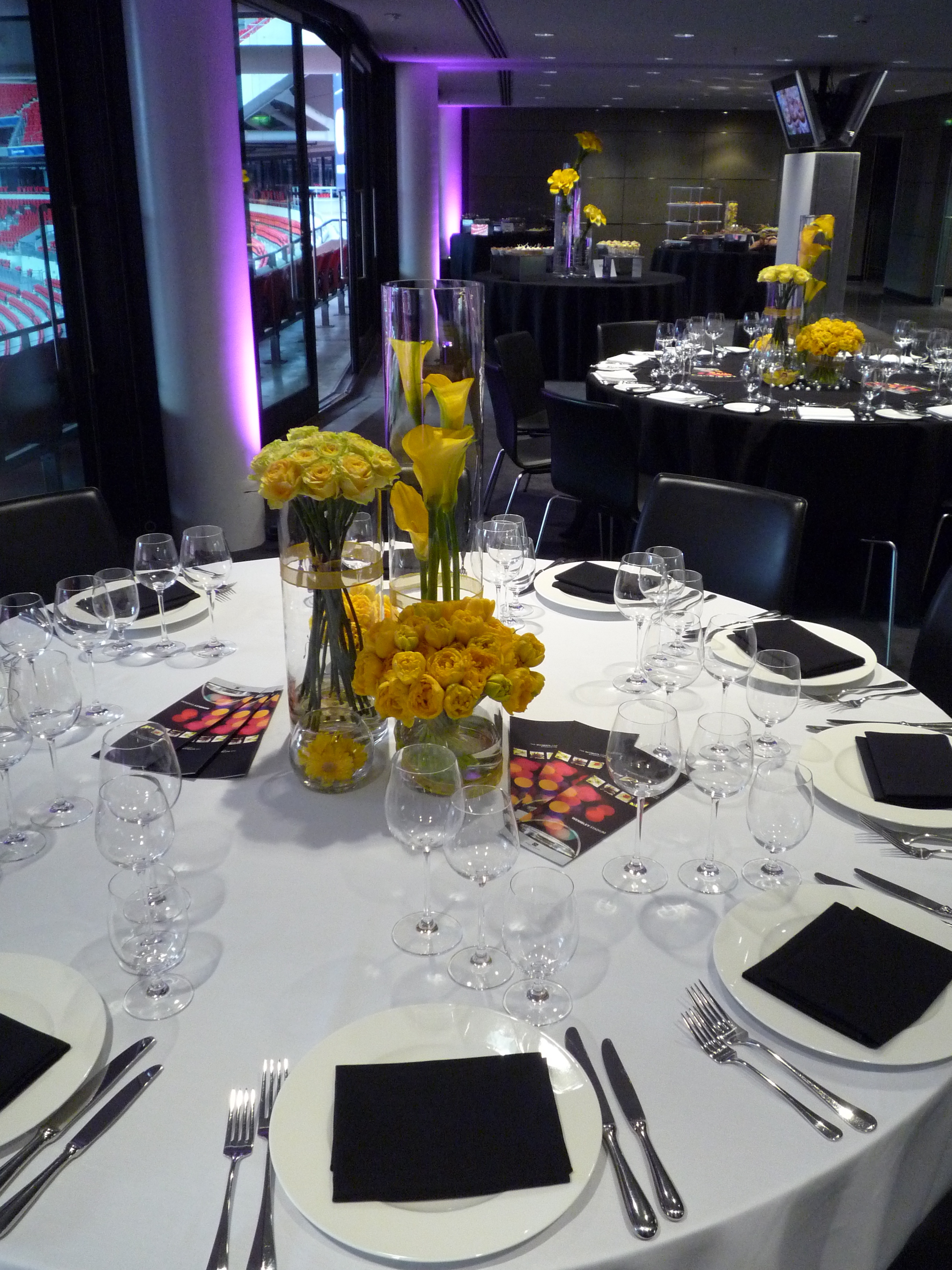 Elegant round table with yellow flowers at Wembley Stadium for corporate events.