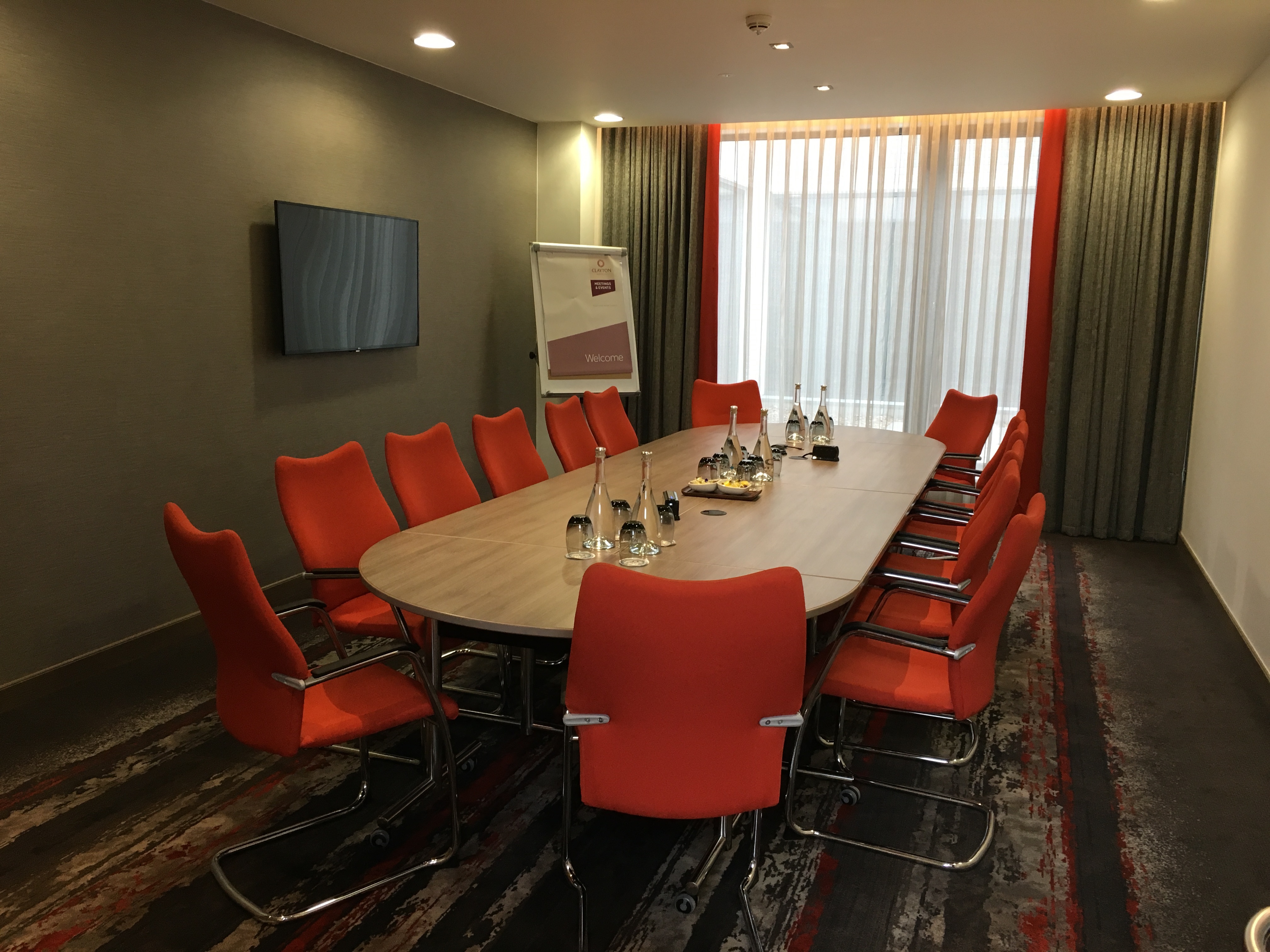 Bedford Suite at Clayton Hotel Chiswick, modern meeting room with oval table and orange chairs.