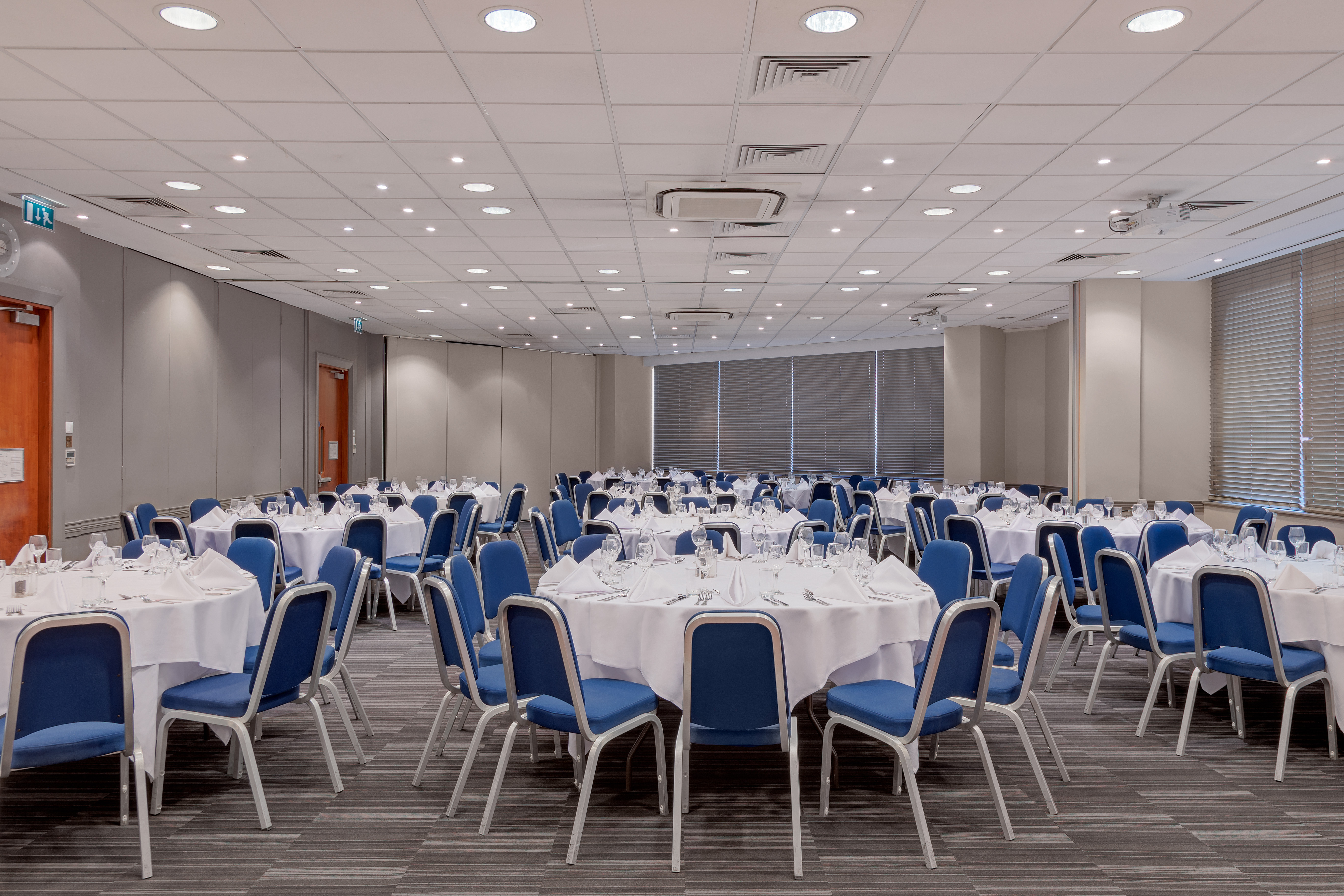 Event space at Holiday Inn London Kensington with round tables and blue chairs.