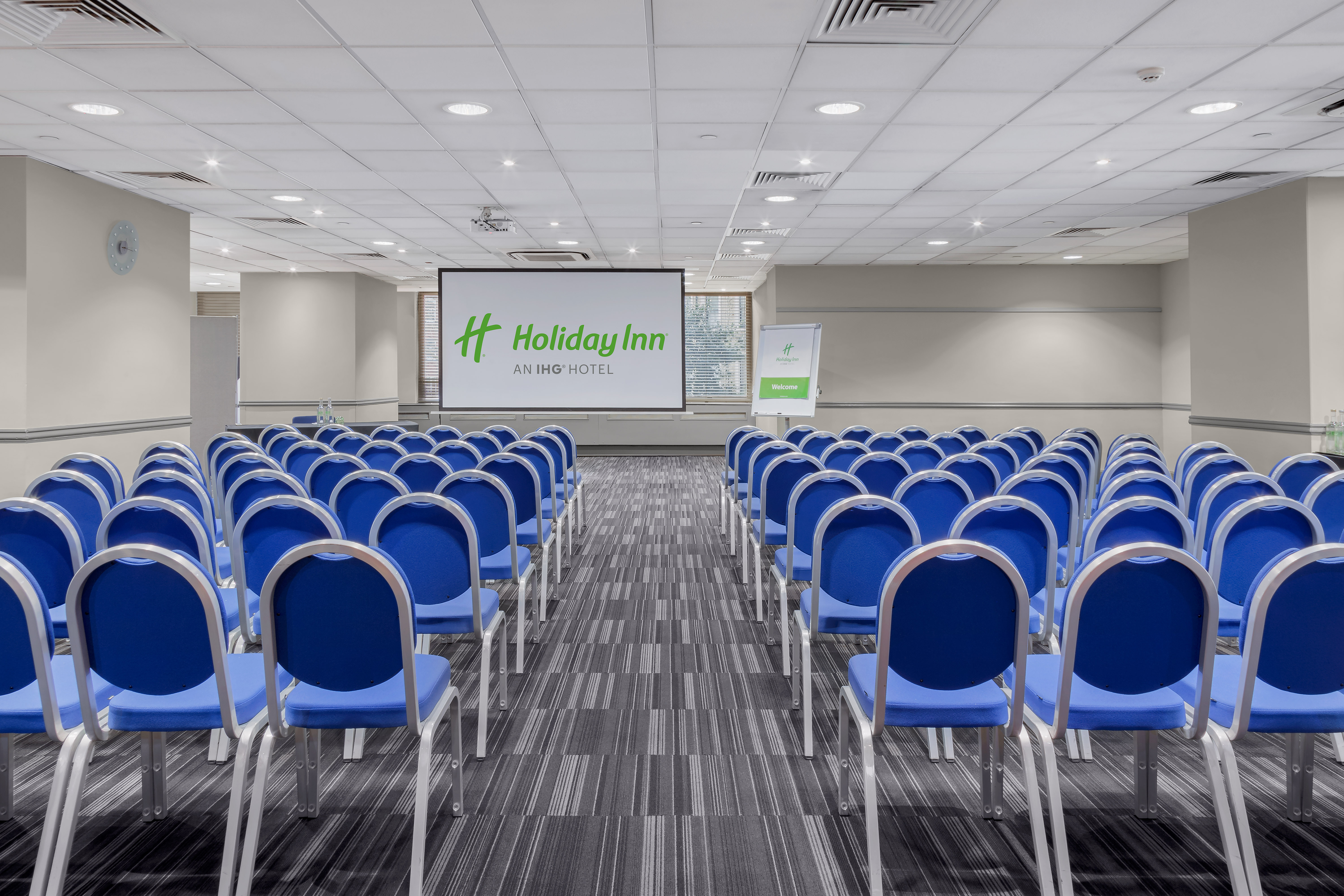 Meeting space with blue chairs and projection screen at Holiday Inn London Kensington.
