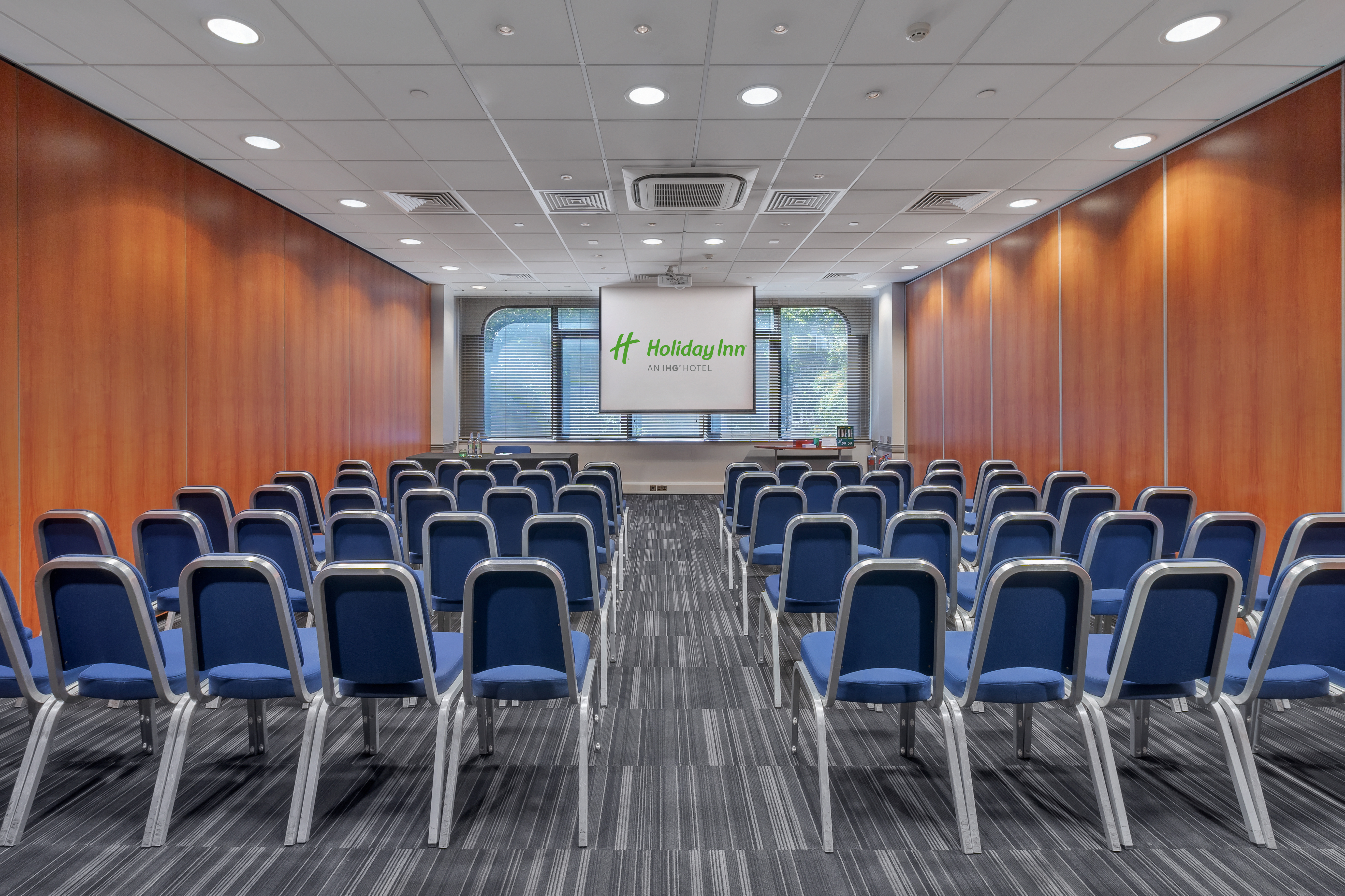 Meeting space with blue chairs and screen at Holiday Inn London Kensington Forum.