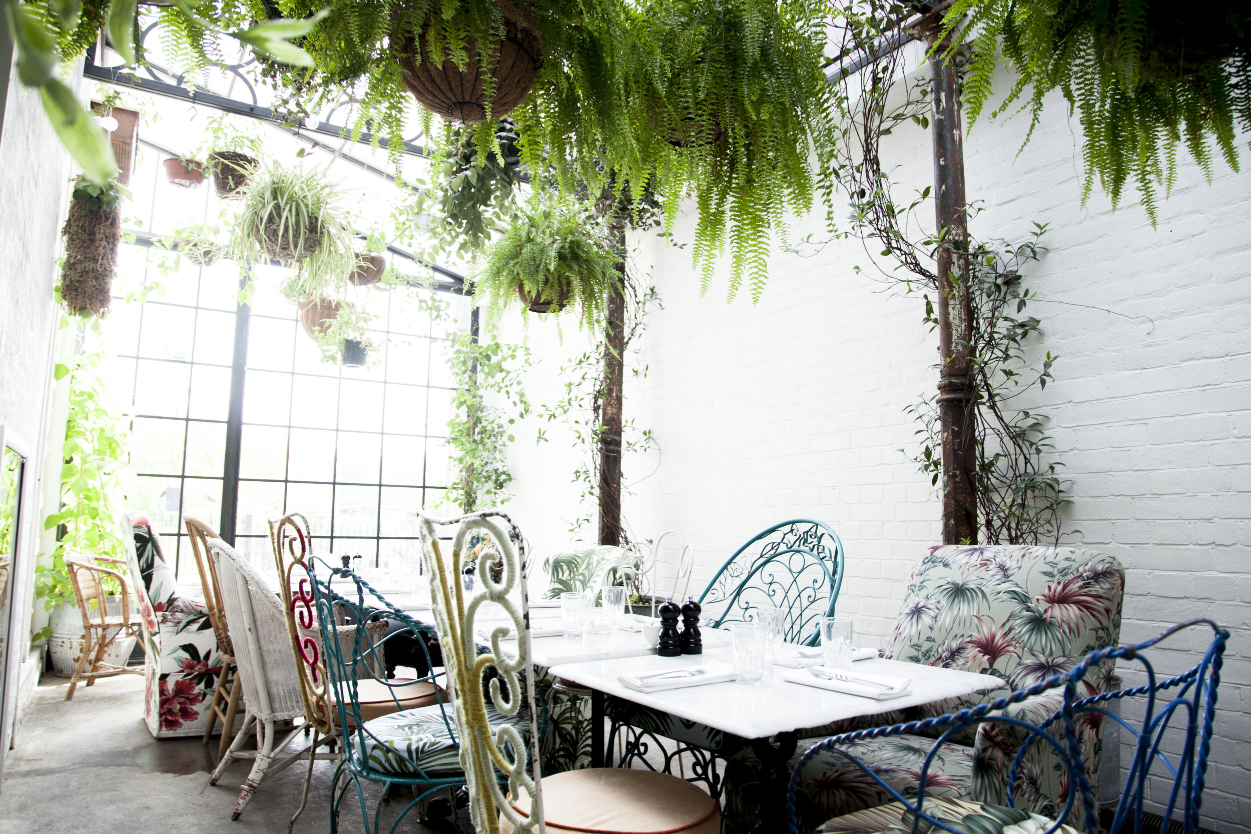 Charming greenhouse dining space with vintage furniture, ideal for brunch events and retreats.