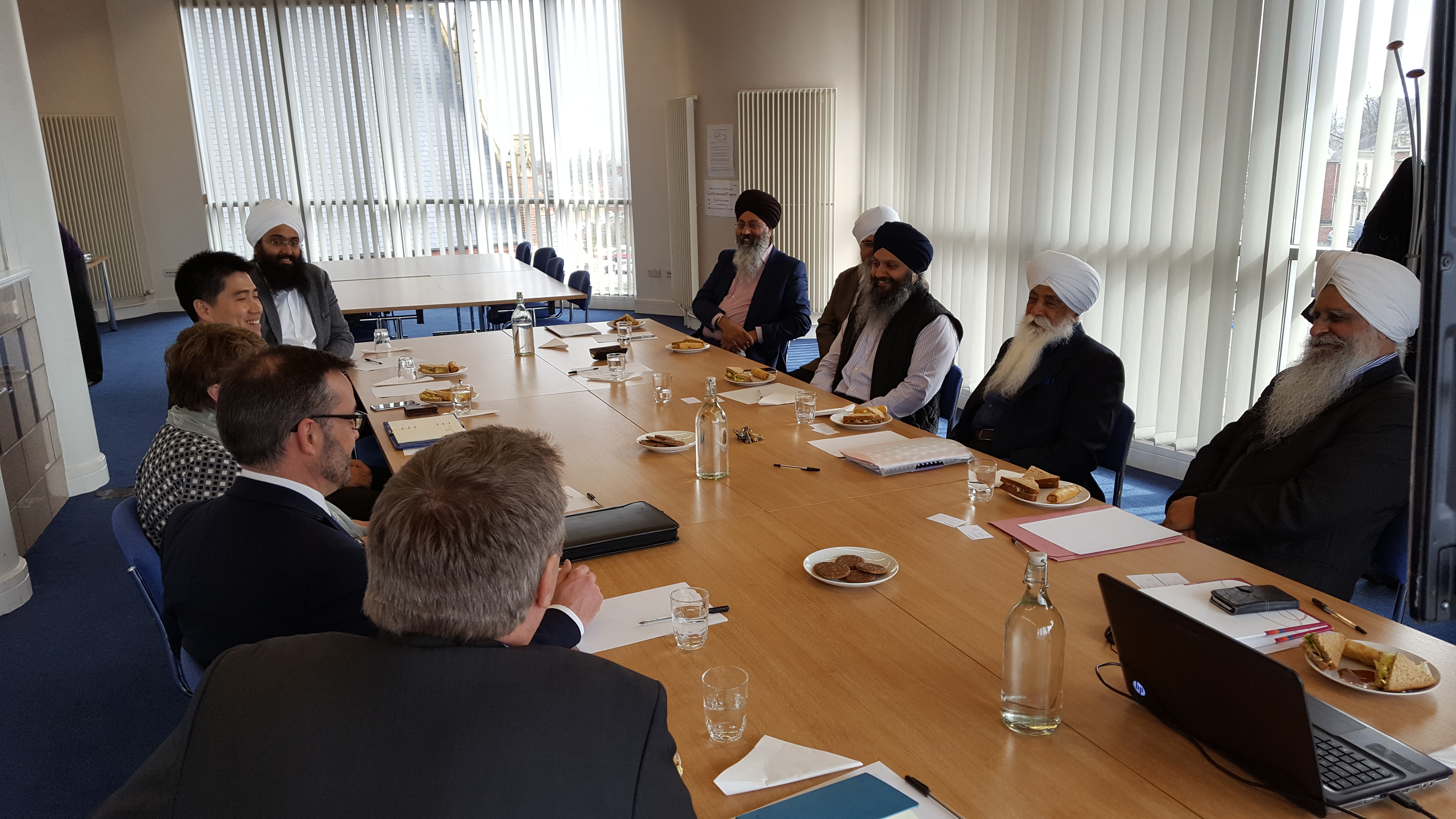 Diverse attendees in formal and traditional attire at Nishkam Centre seminar room meeting.