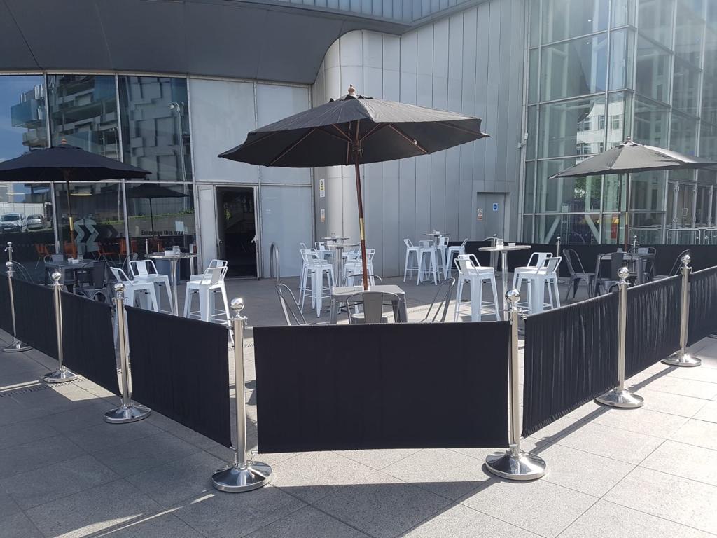 Outdoor event space at INGRESS, featuring tables under black umbrellas for networking.