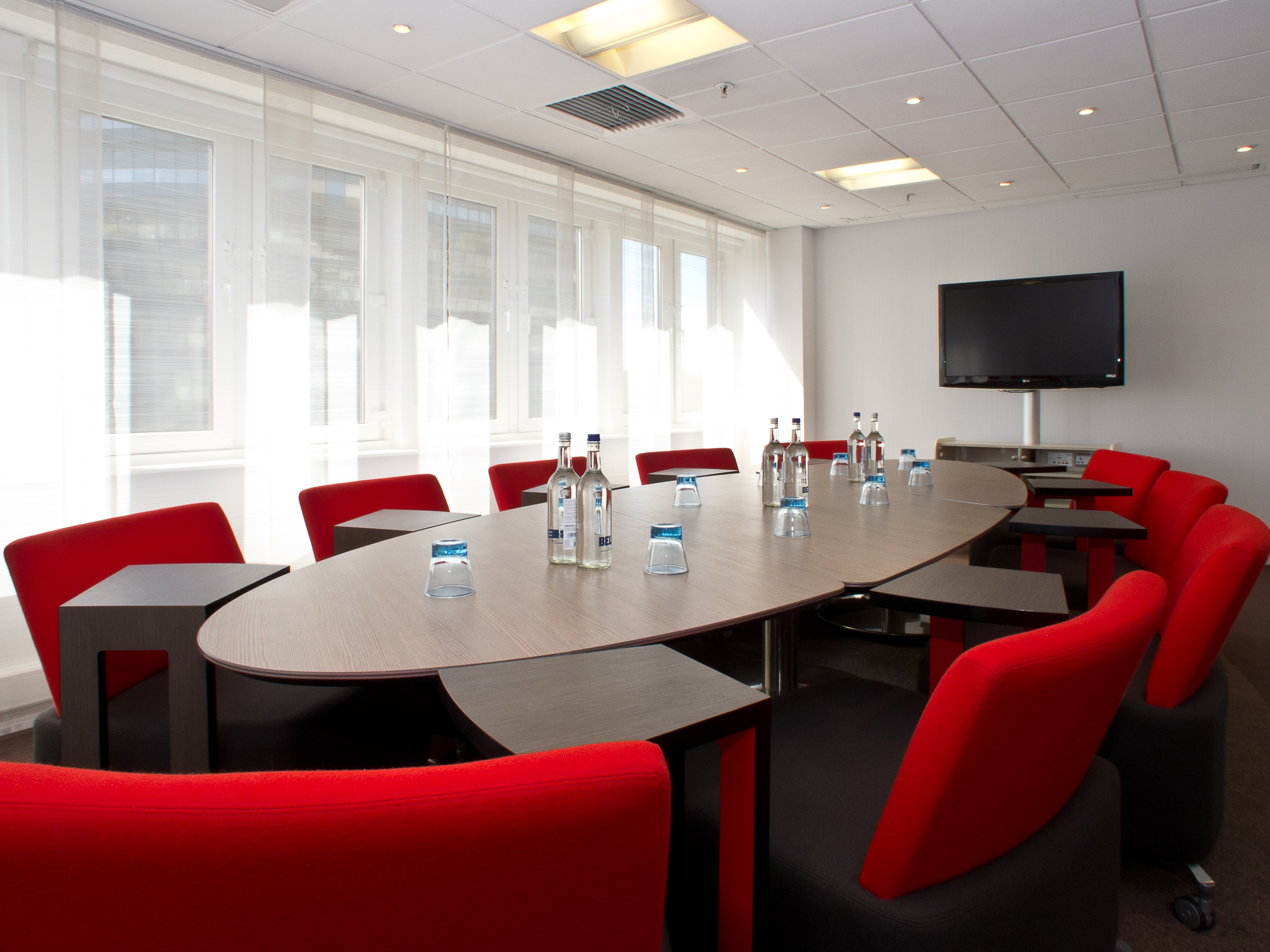 Modern meeting room with oval table and red chairs at Novotel London West.