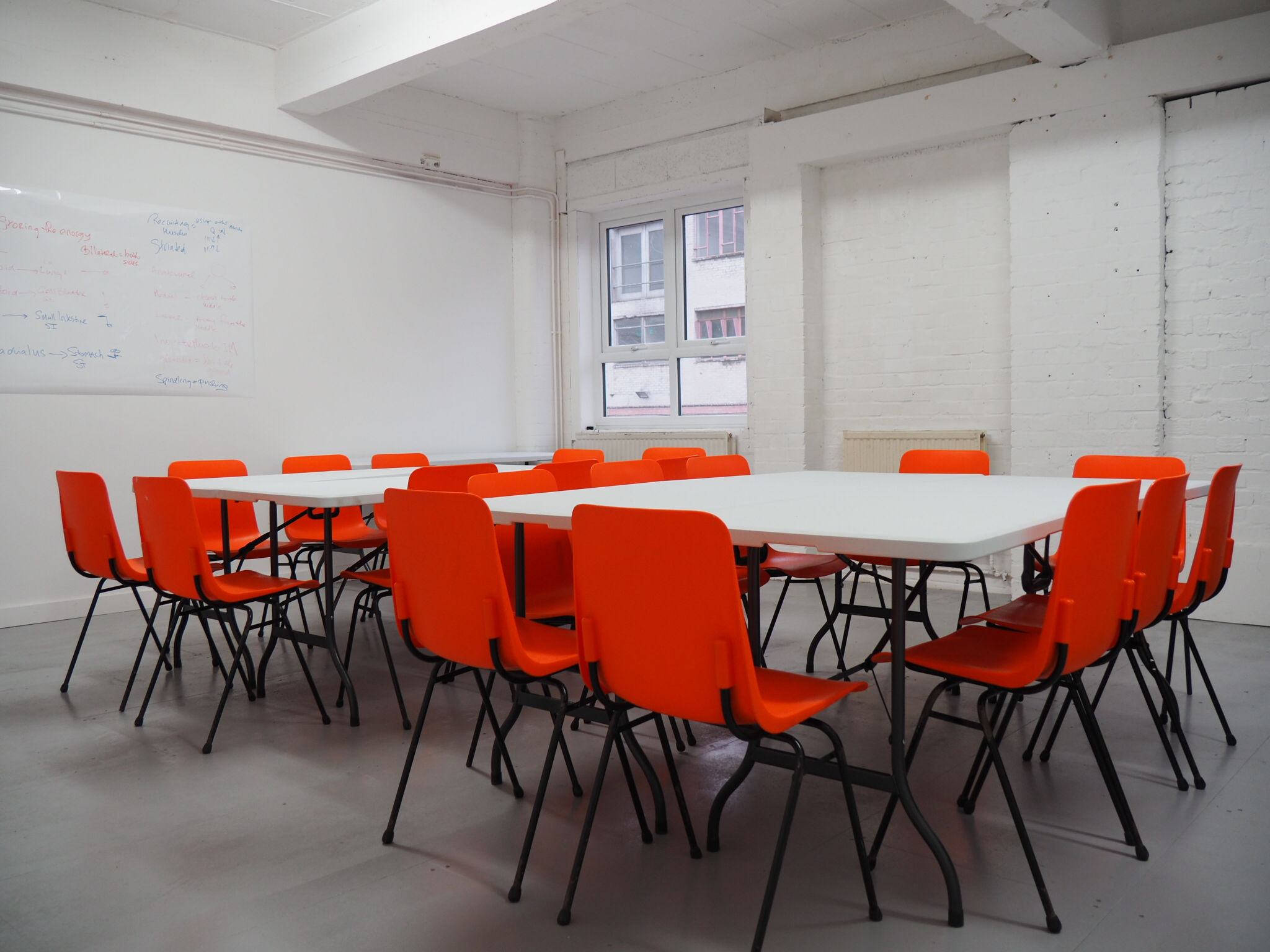 Versatile meeting space with large table and bright orange chairs for collaborative workshops.