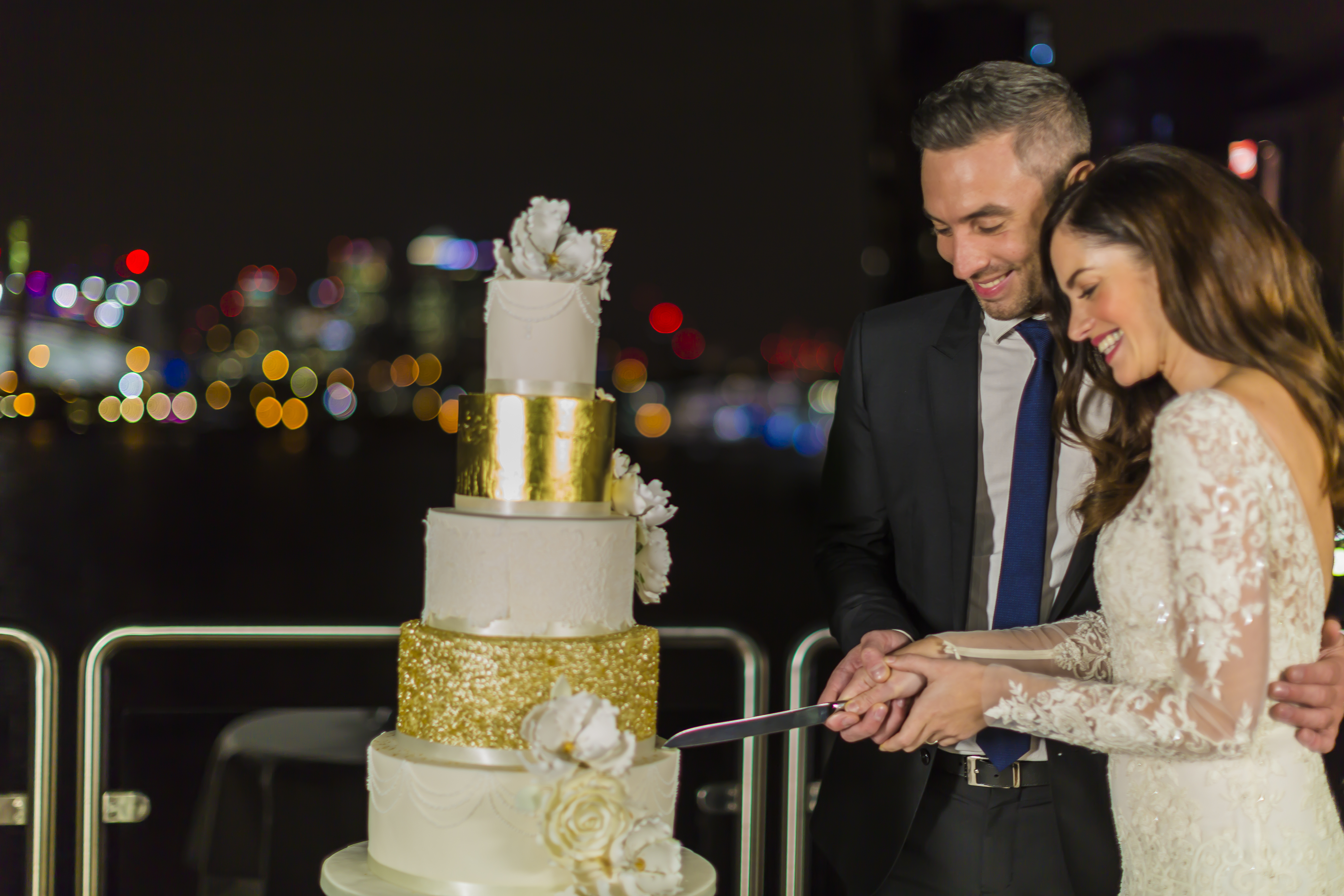 Couple cutting wedding cake at Sunborn London Yacht Hotel with city skyline backdrop.
