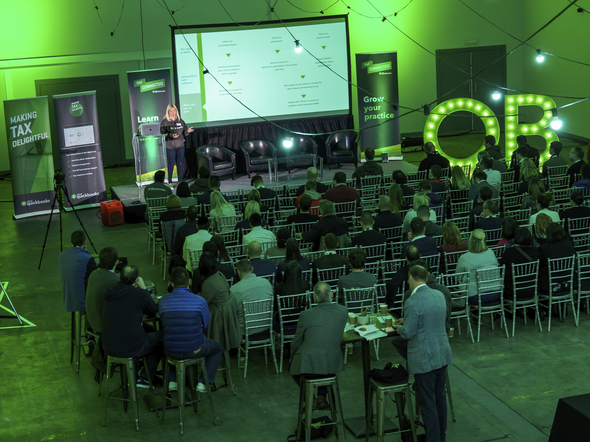 Event Hall conference with presenter, green lighting, and engaging atmosphere.