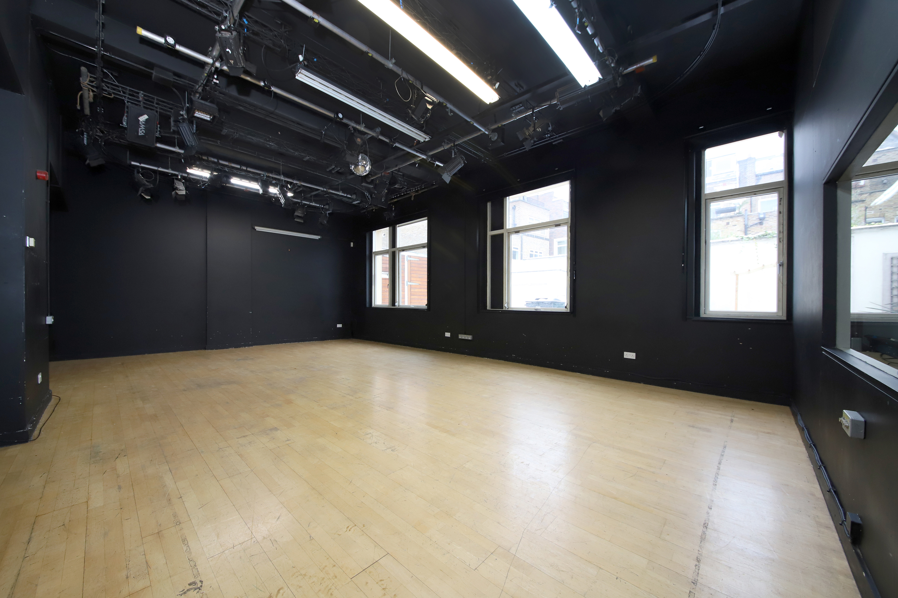 Versatile event space with black walls and natural light, ideal for workshops and performances.