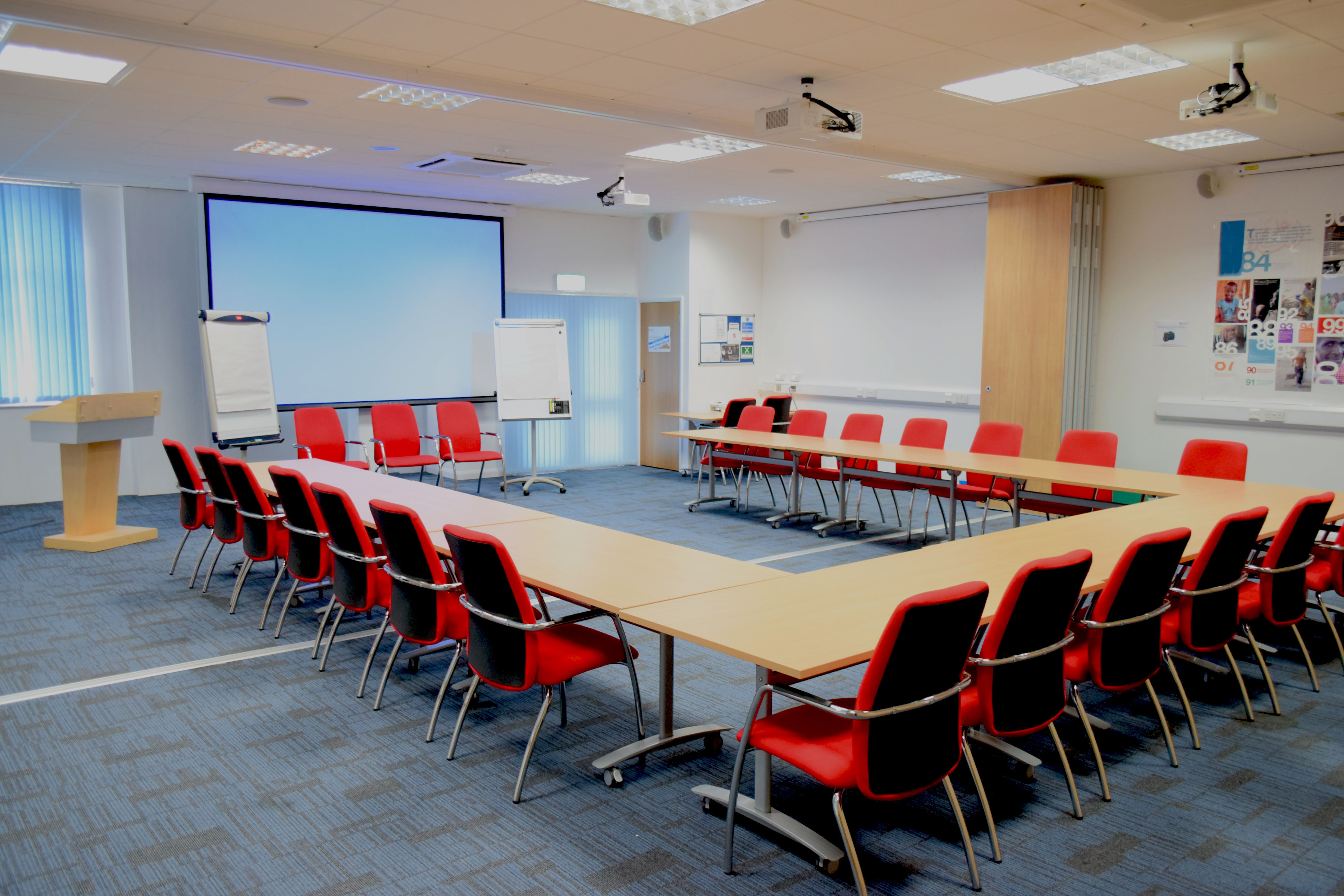 Conference room with U-shaped table, red chairs for workshops and strategic planning.