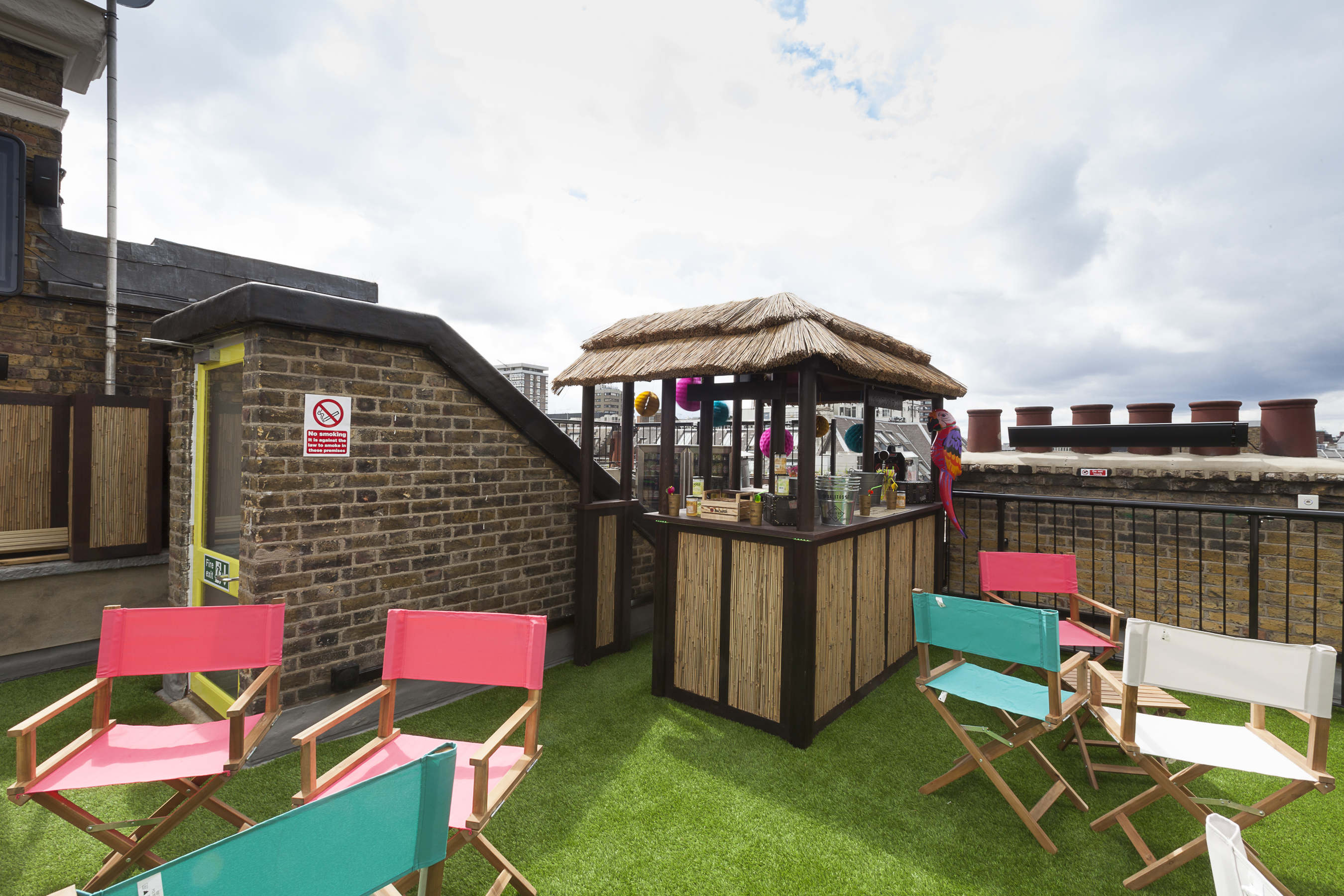 Vibrant rooftop event space with thatched bar and colorful seating for summer parties.