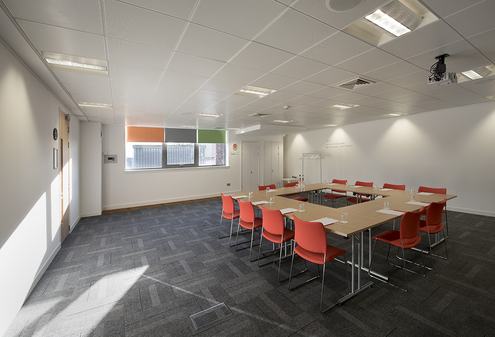 Well-lit meeting room at Aspire Glasgow with large table and orange chairs for collaboration.