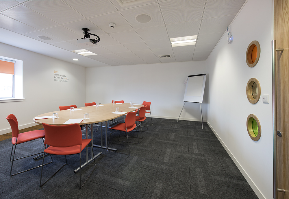 Modern meeting room at Twist in Glasgow with round table and orange chairs for collaboration.