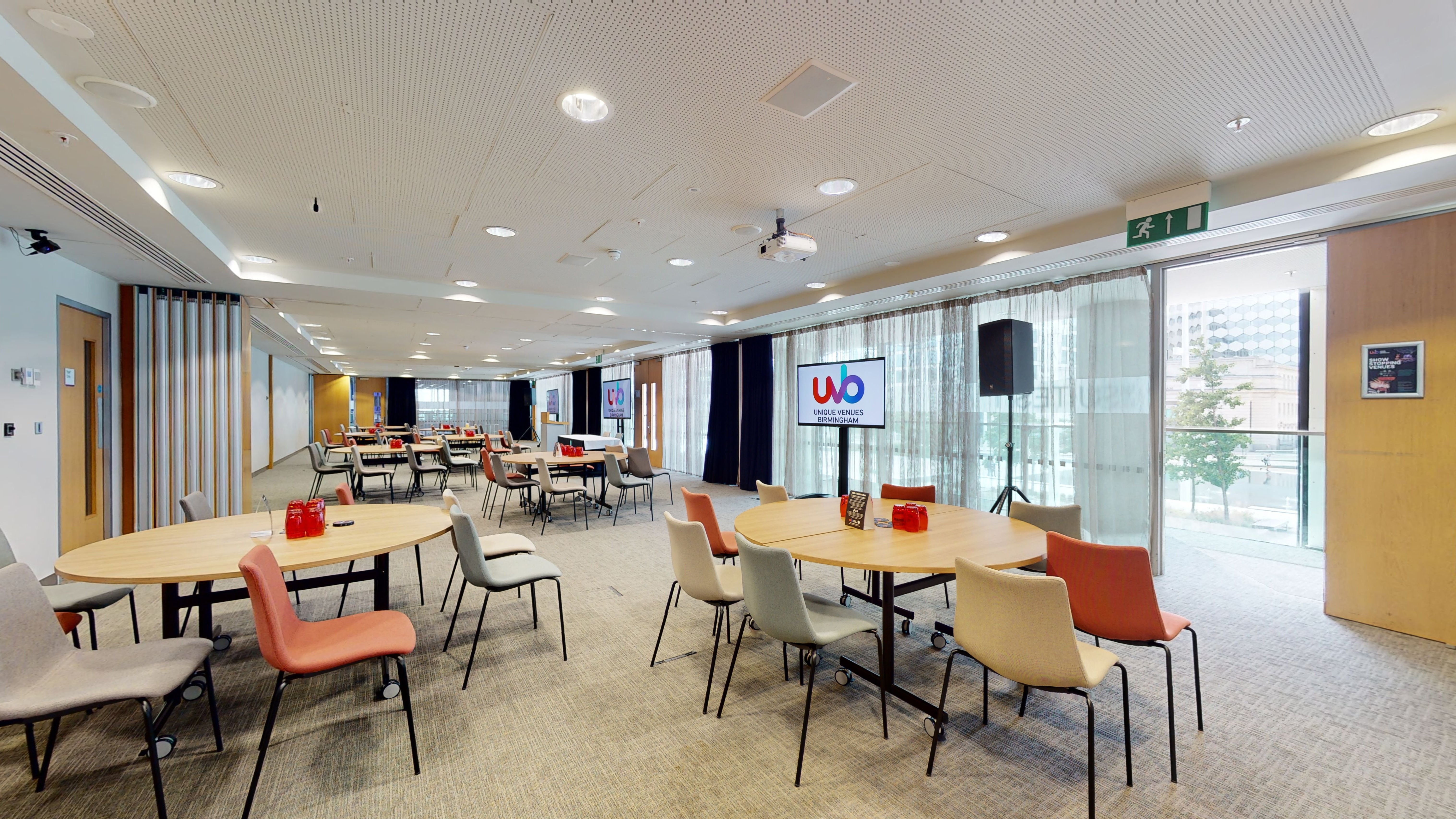 Versatile meeting room with round tables and AV setup for workshops and networking events.