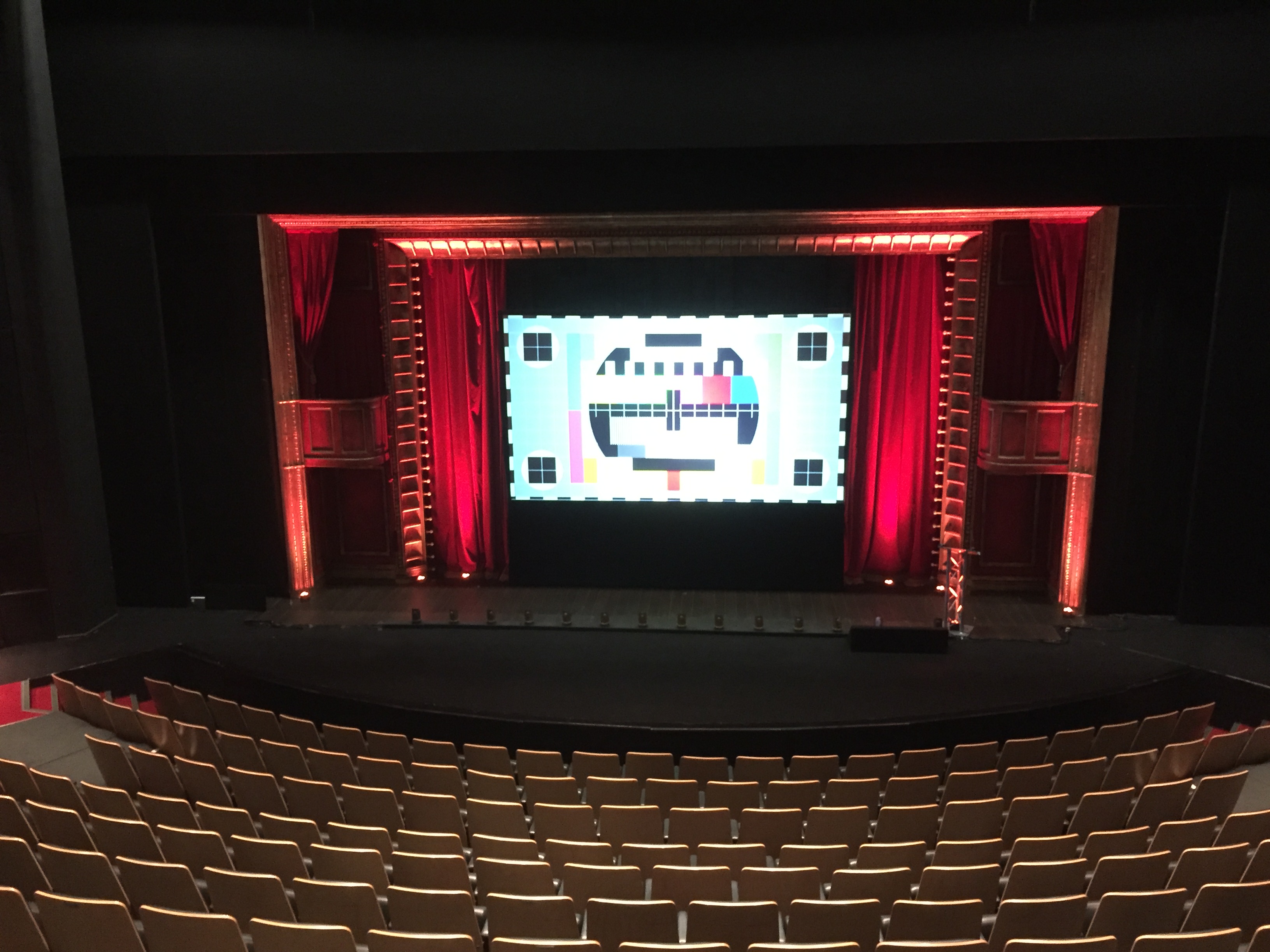 Theater space with large screen and red curtains, perfect for conferences and events.
