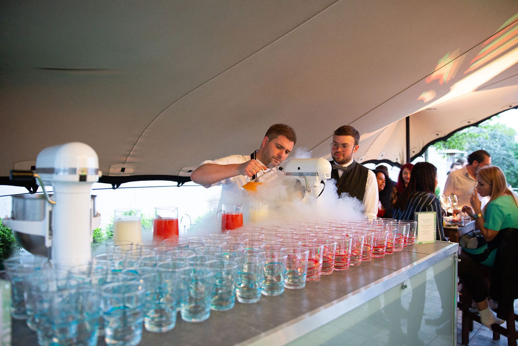 Outdoor summer party beverage station with colorful cocktails and dry ice effects.