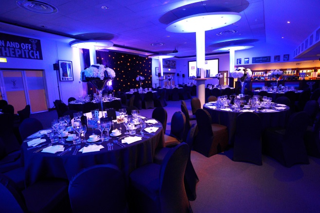 Elegant gala setup with round tables and blue lighting at Twickenham Stoop Stadium.
