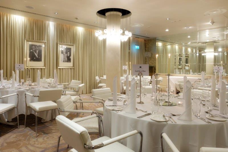 Elegant dinner setup in Hard Days Night Hotel with round tables and soft chandelier lighting.