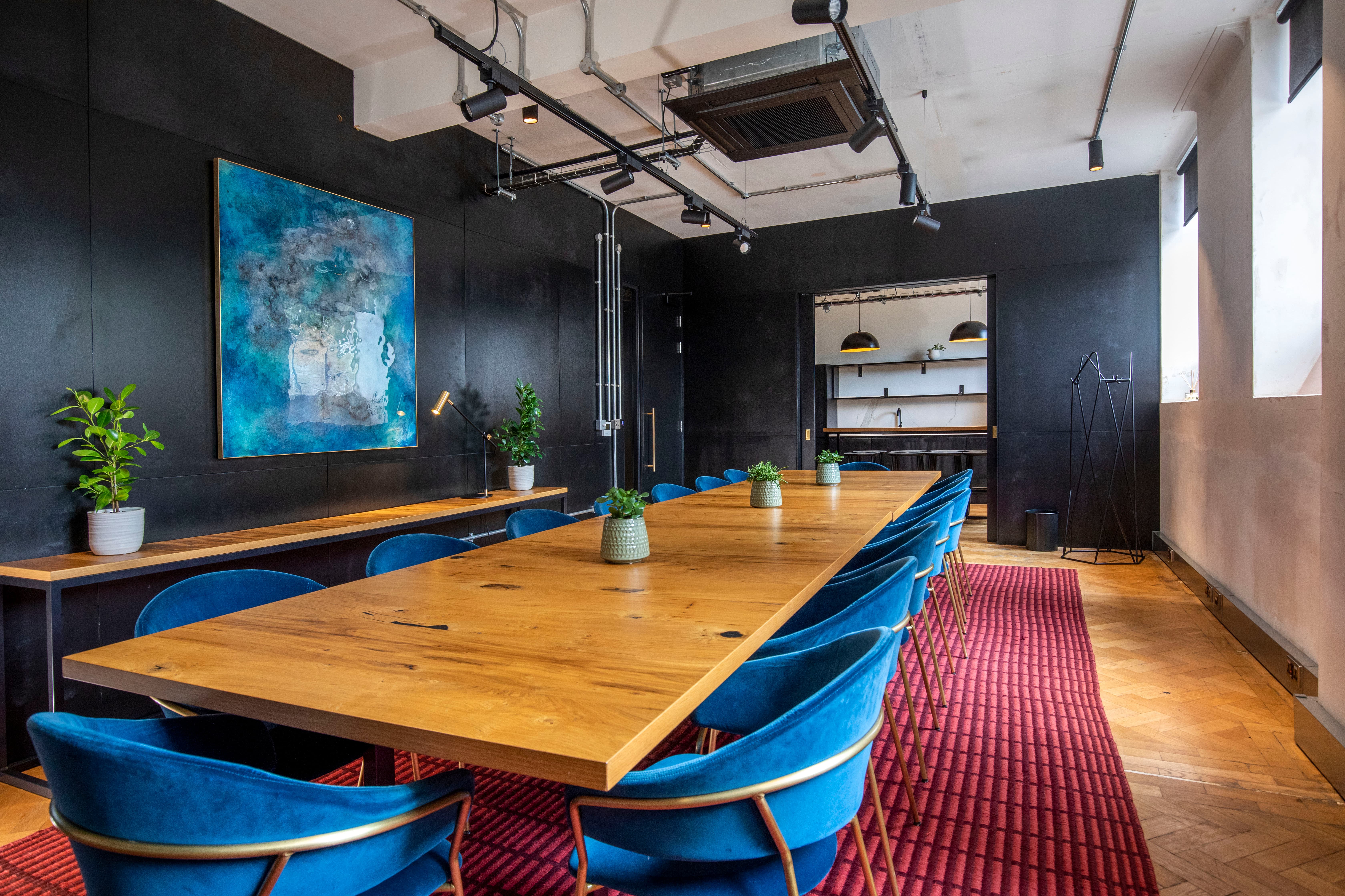 Modern boardroom with black walls and blue velvet chairs for creative meetings and executive events.