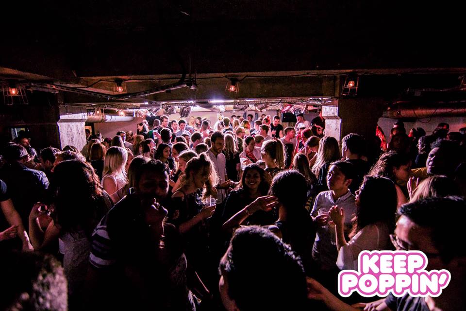 Vibrant crowd at underground venue event with dim lighting and "Keep Poppin'" branding.