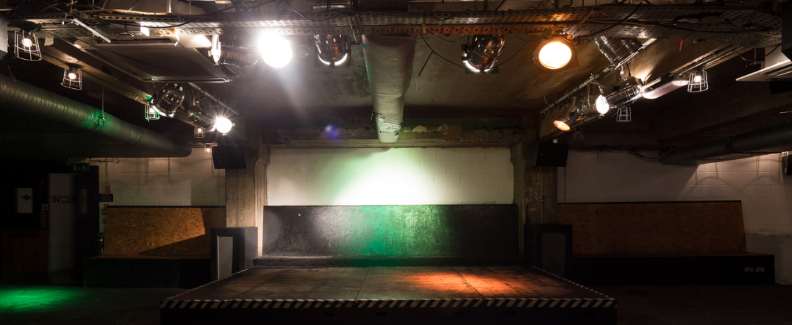 Versatile industrial event space with adjustable stage lighting for presentations and performances.