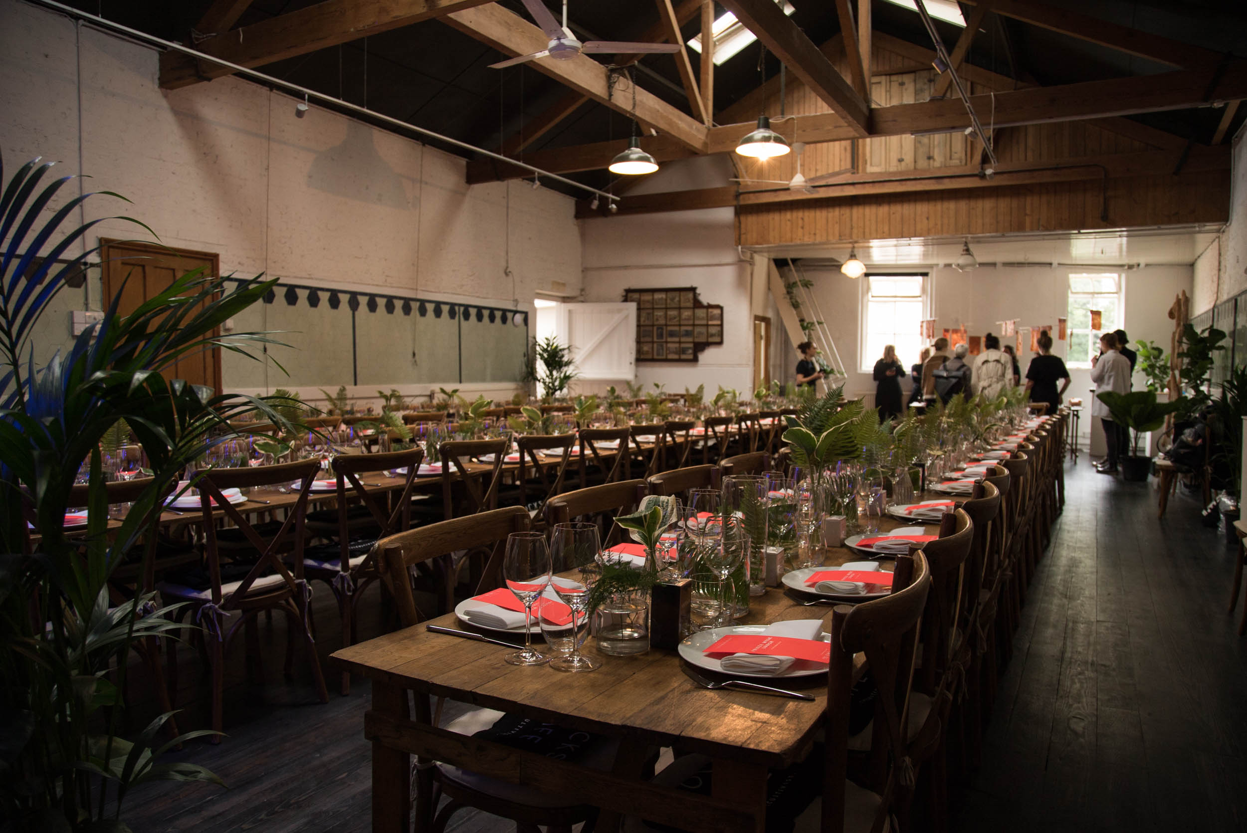 Elegant event space at The Stables, featuring long wooden tables and lush greenery.