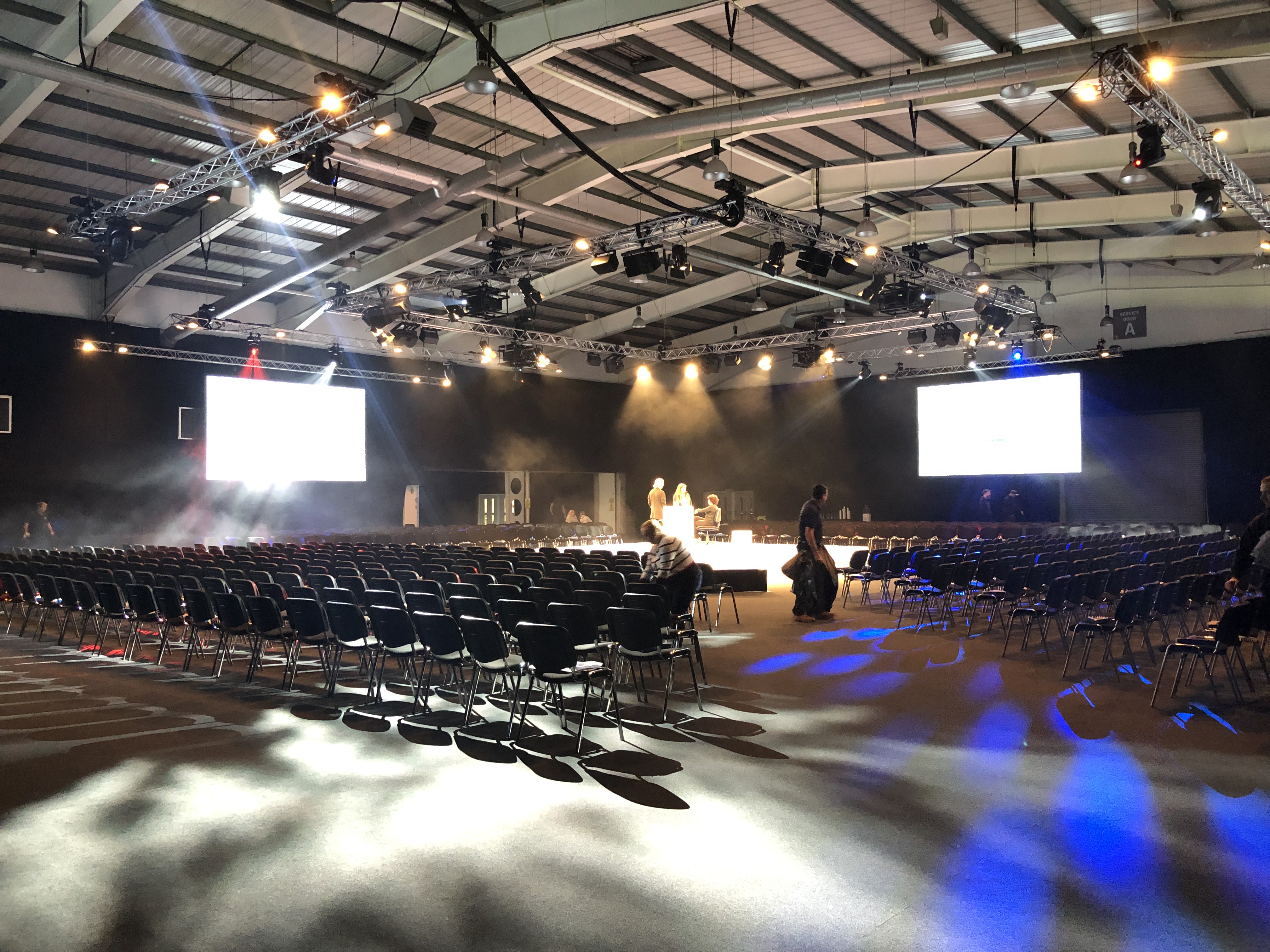 Spacious NAEC Stoneleigh conference hall with black chairs and dramatic lighting.