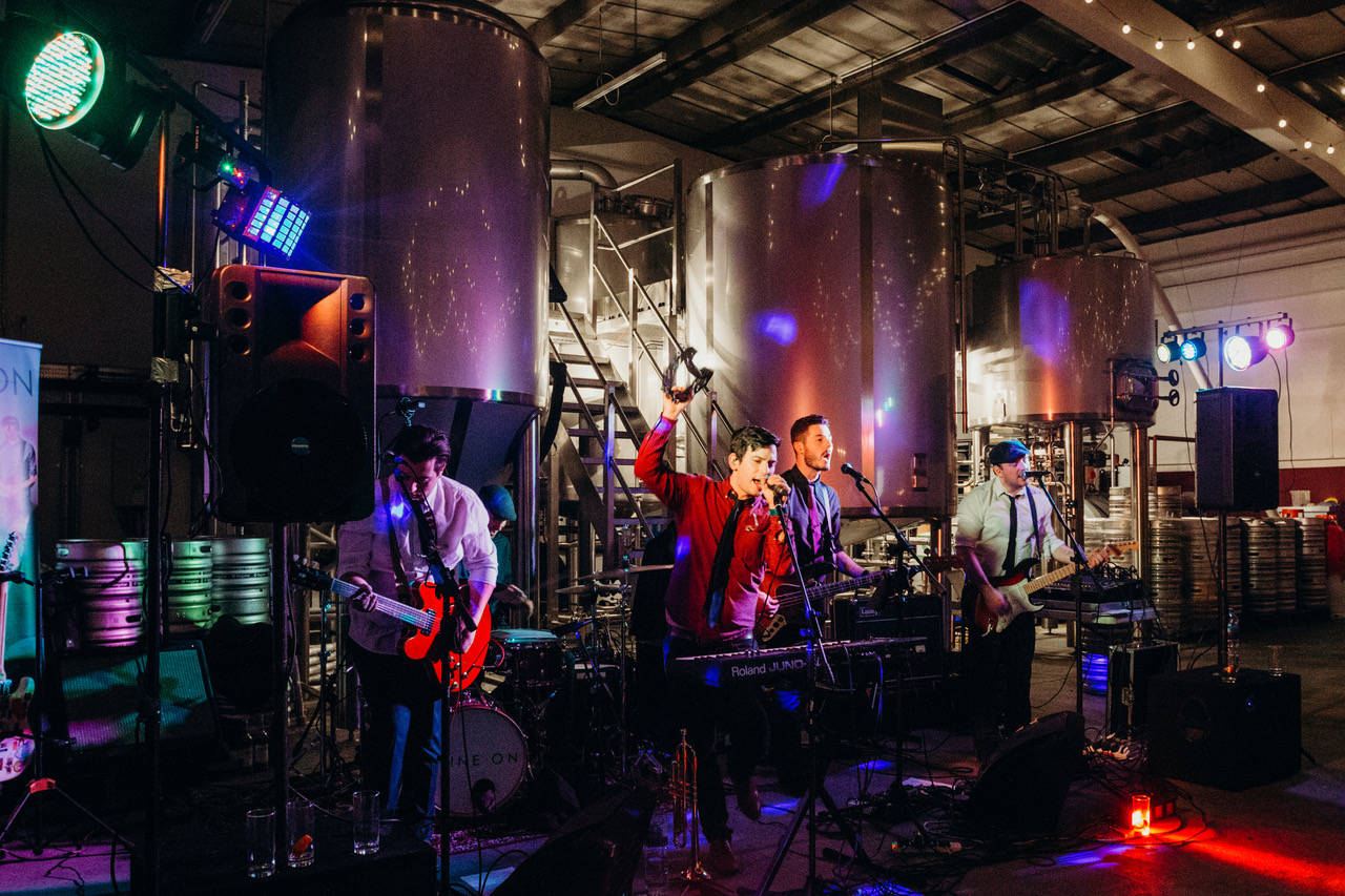 Live band performing in Small Beer Brewery's vibrant Main Brew Room with fermentation tanks.