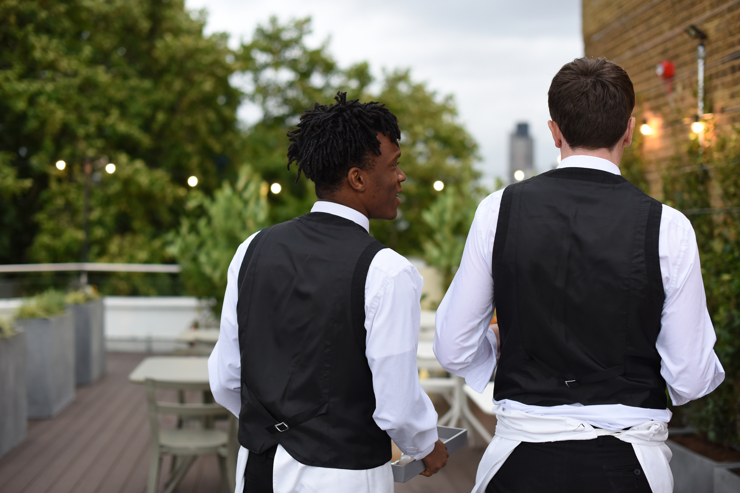 Professional waitstaff on rooftop terrace, preparing for elegant event with greenery.