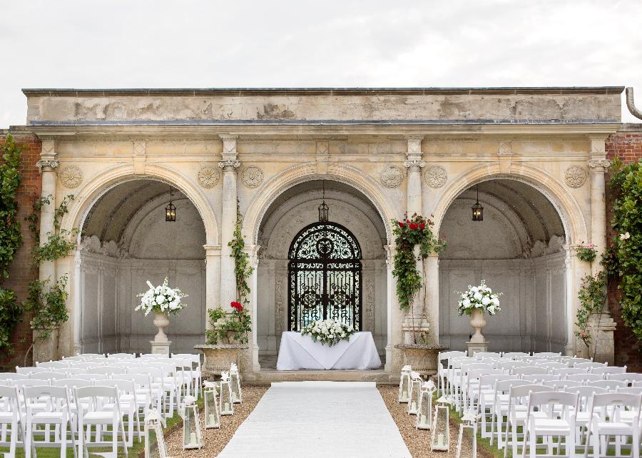 Elegant outdoor wedding venue at The Mansion House, featuring floral archway and chairs.