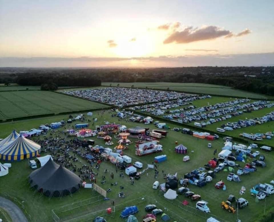 Outdoor festival at Ashley Showground with colorful tents and sunset backdrop.