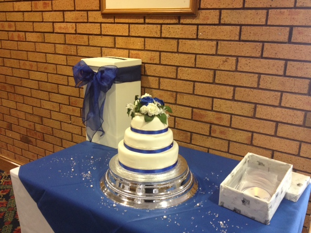 Wedding cake display at Springfield Lounge, DW Stadium, with floral decor and blue accents.