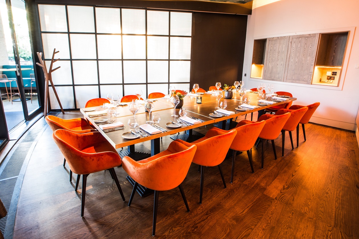 Private dining room with modern table and orange chairs, perfect for gatherings or meetings.