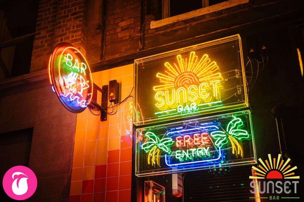 Vibrant Sunset Bar entrance with neon signs, ideal for casual gatherings and events.