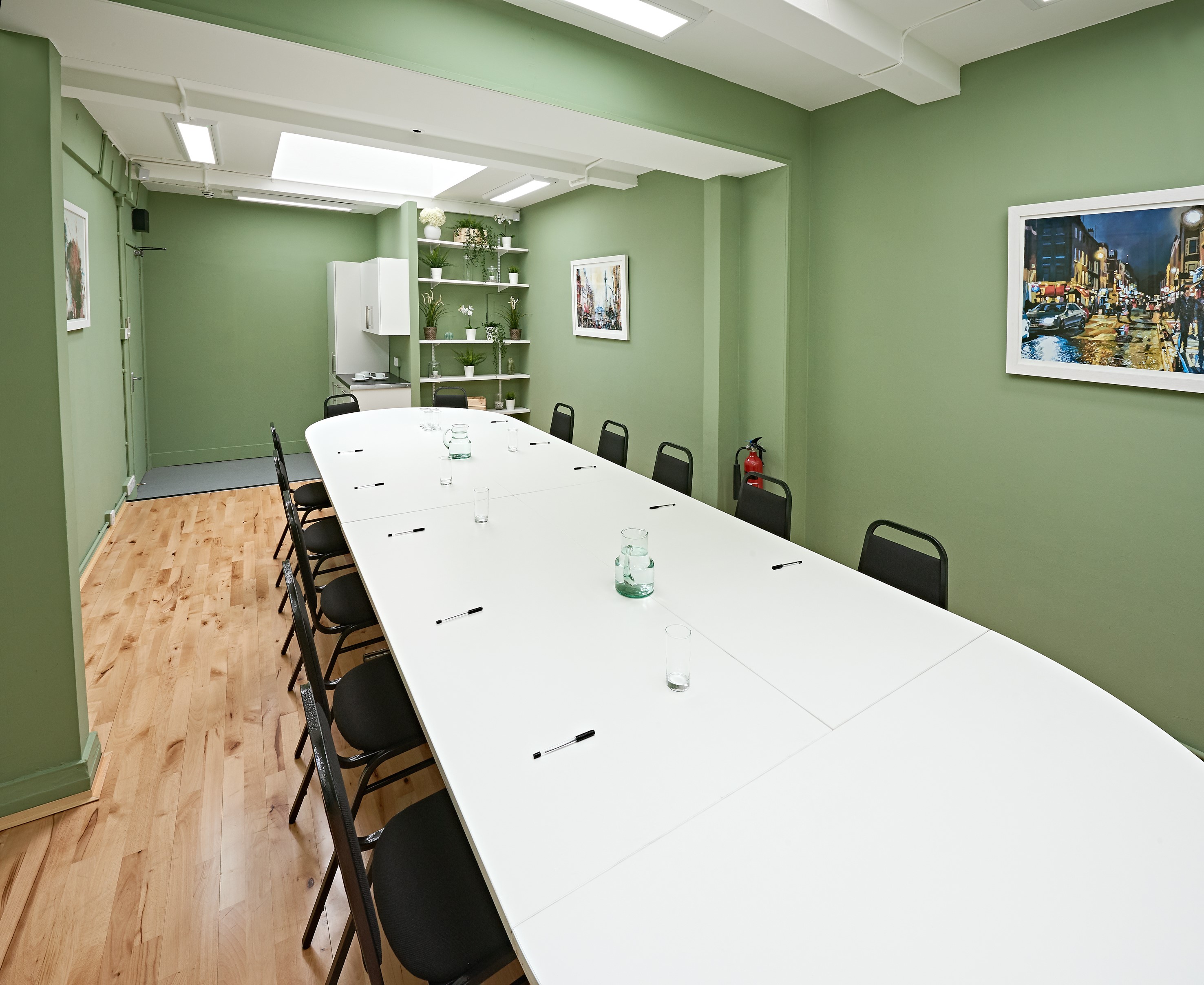 Modern meeting room at The Whitehall Studio, featuring a long white table and green walls.