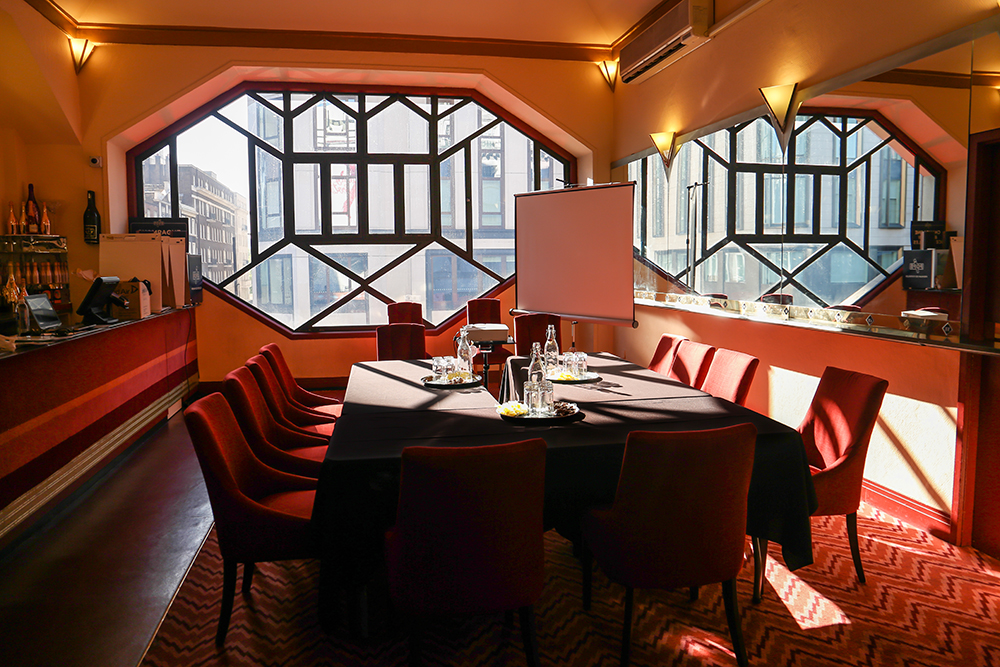 Dress Circle Bar at Adelphi Theatre: elegant meeting room with plush red chairs, ideal for corporate events.