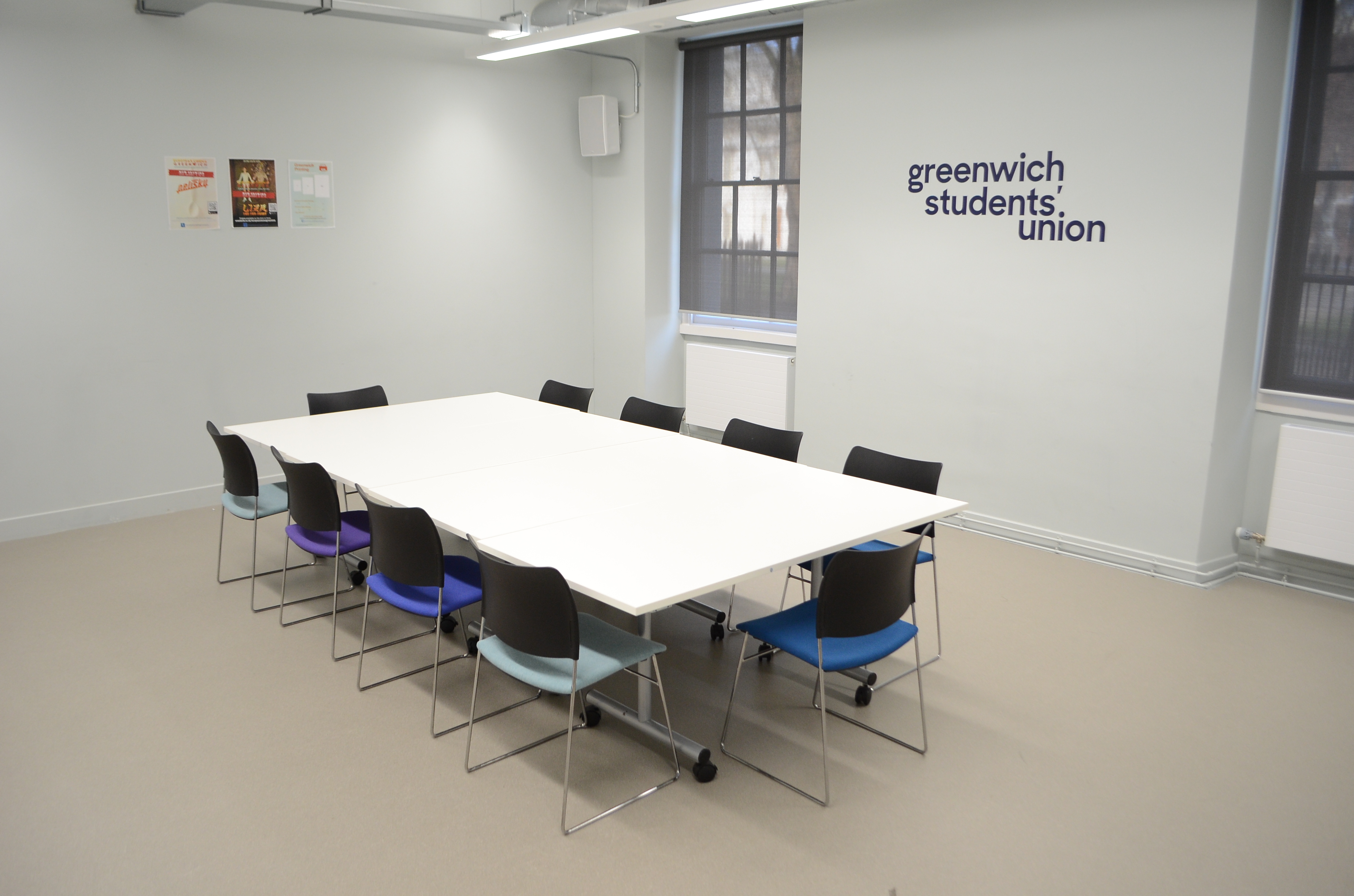 Modern meeting room with large white table, colorful chairs for workshops and collaboration.