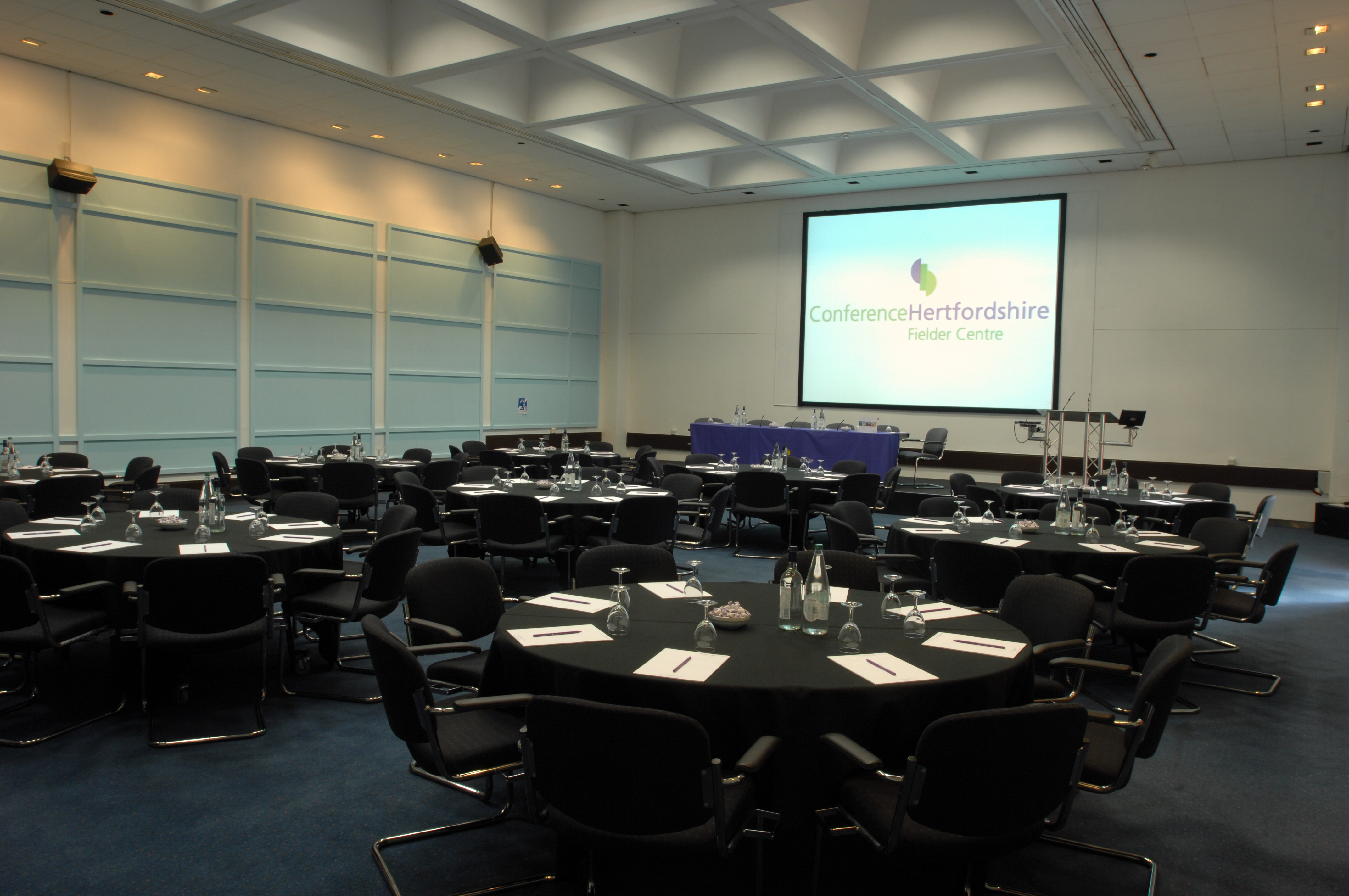 Conference room with round tables, AV tech, ideal for corporate events and workshops.