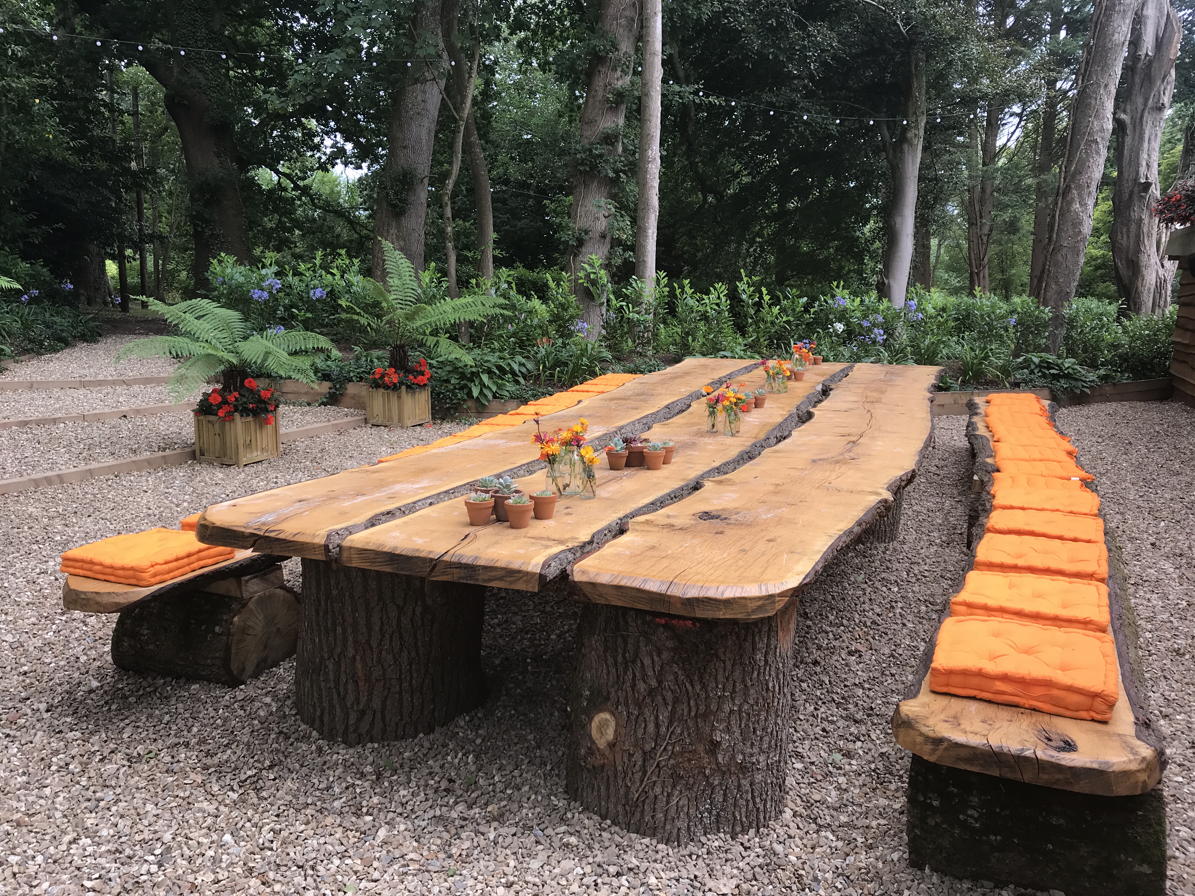 Rustic outdoor meeting setup with wooden table and log seating in Deer Park Gardens.