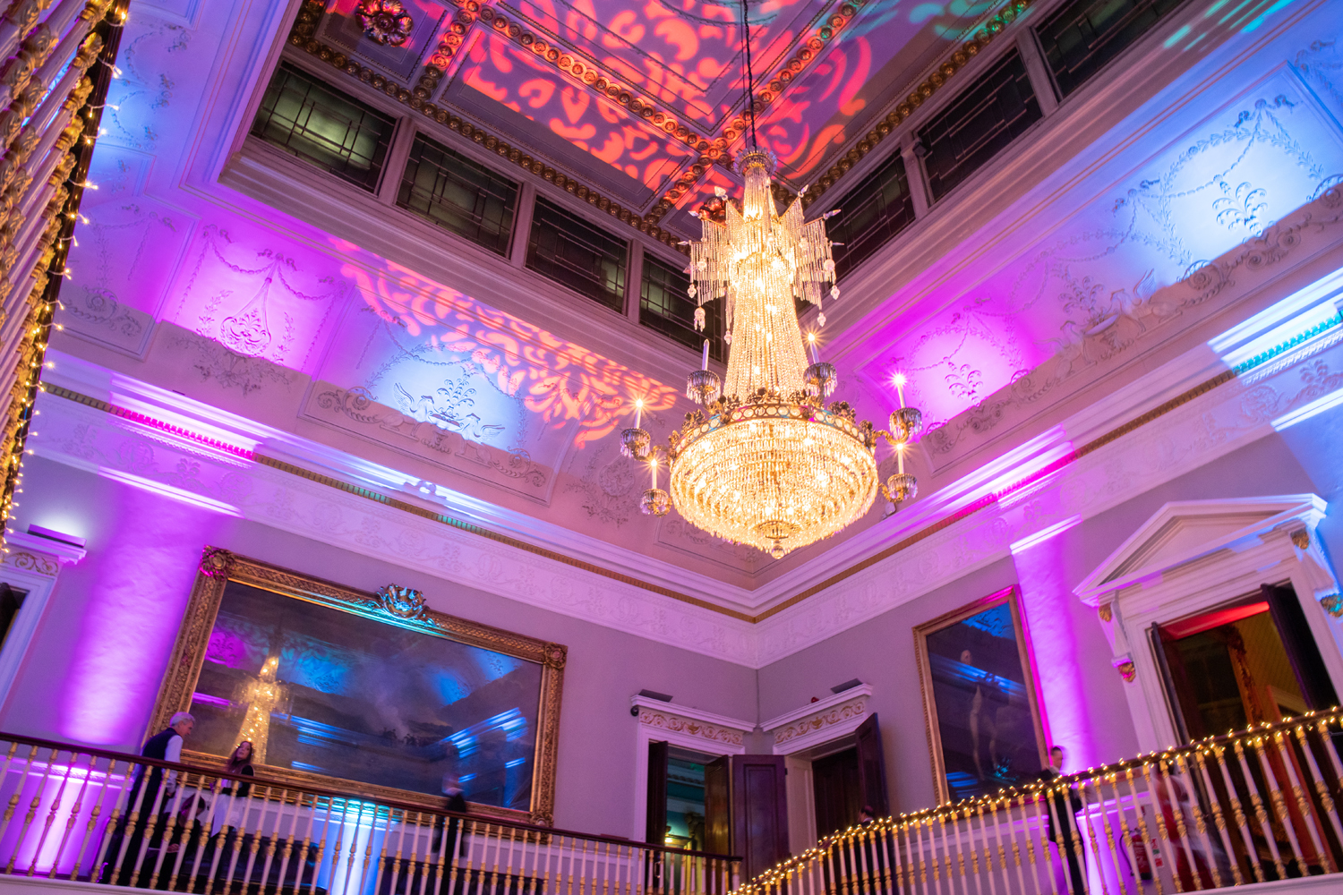 Elegant Trafalgar Rooms event space with chandelier and vibrant uplighting for celebrations.