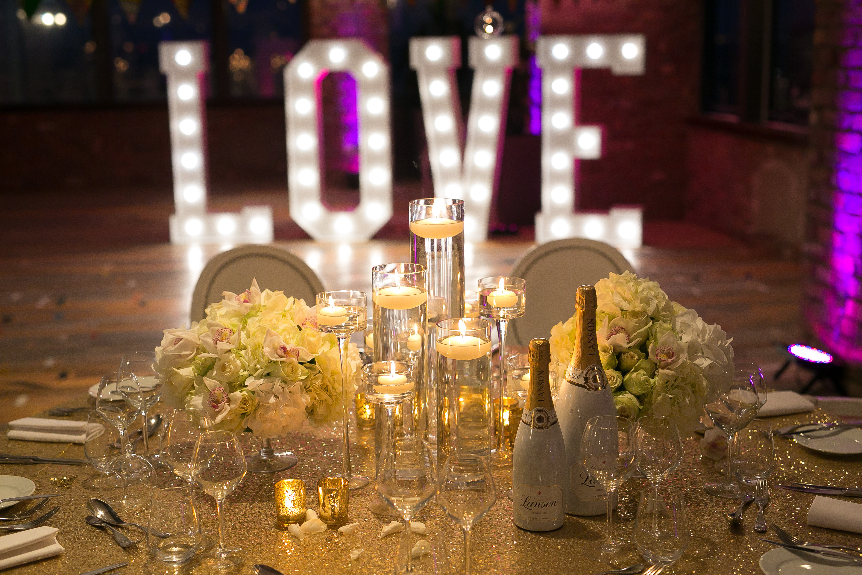 Elegant wedding table with floral centerpieces and illuminated "LOVE" letters.