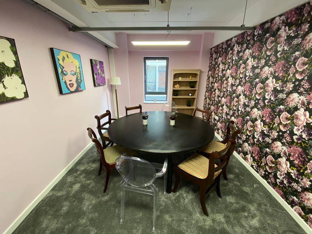 Cozy meeting space with round black table, vibrant floral wallpaper, ideal for brainstorming.
