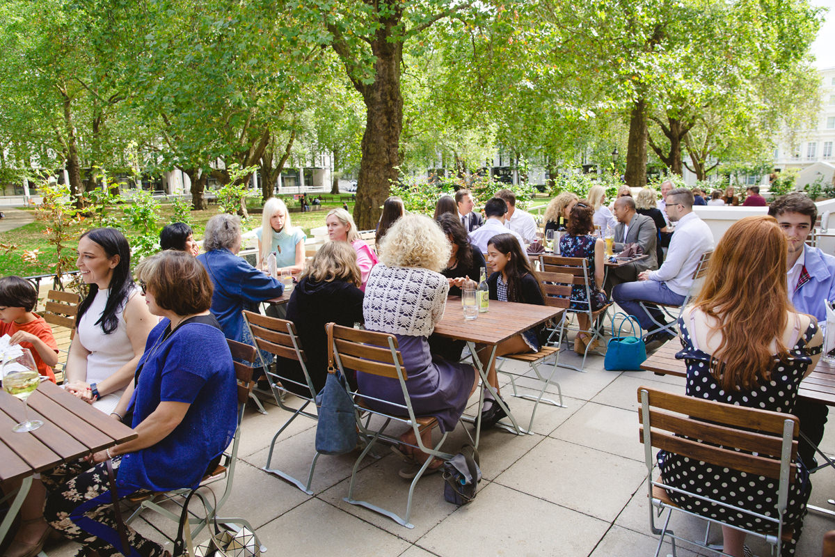 Outdoor networking event at Stein's Berlin Restaurant Terrace with wooden tables and lush trees.