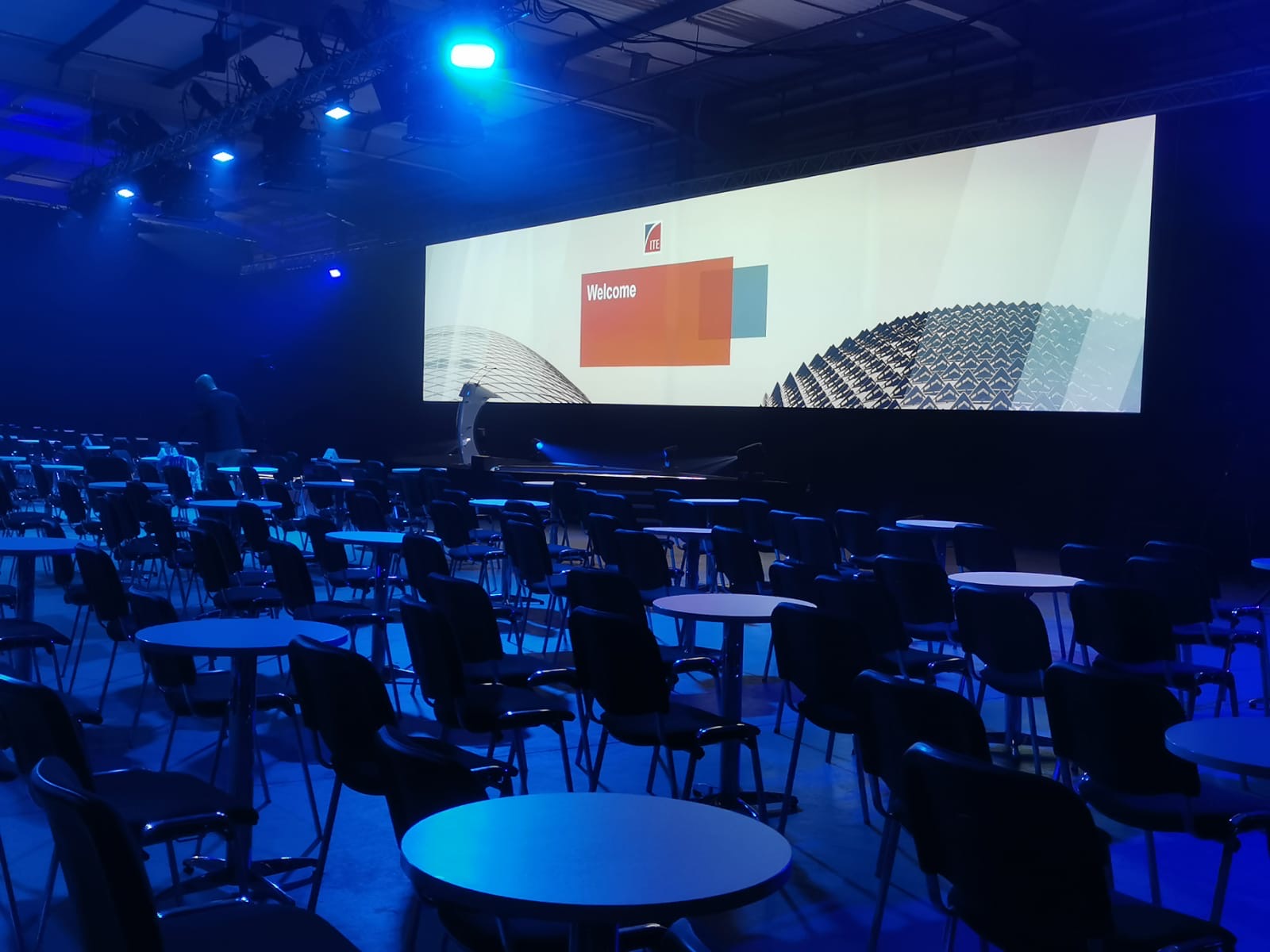 Spacious Dock X London venue set for meetings with blue lighting and presentation screen.