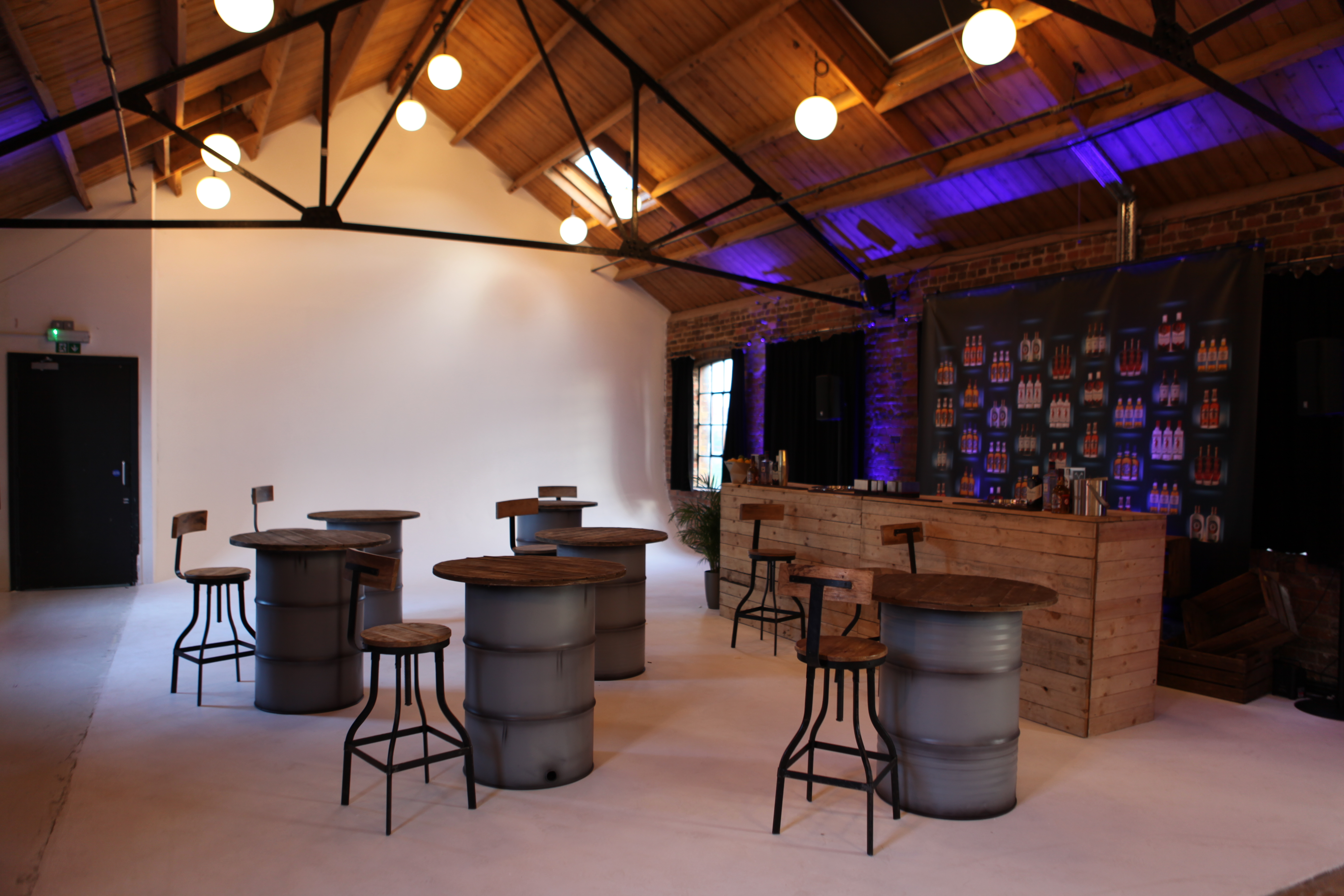 Versatile industrial event space with barrel tables, ideal for networking and receptions.