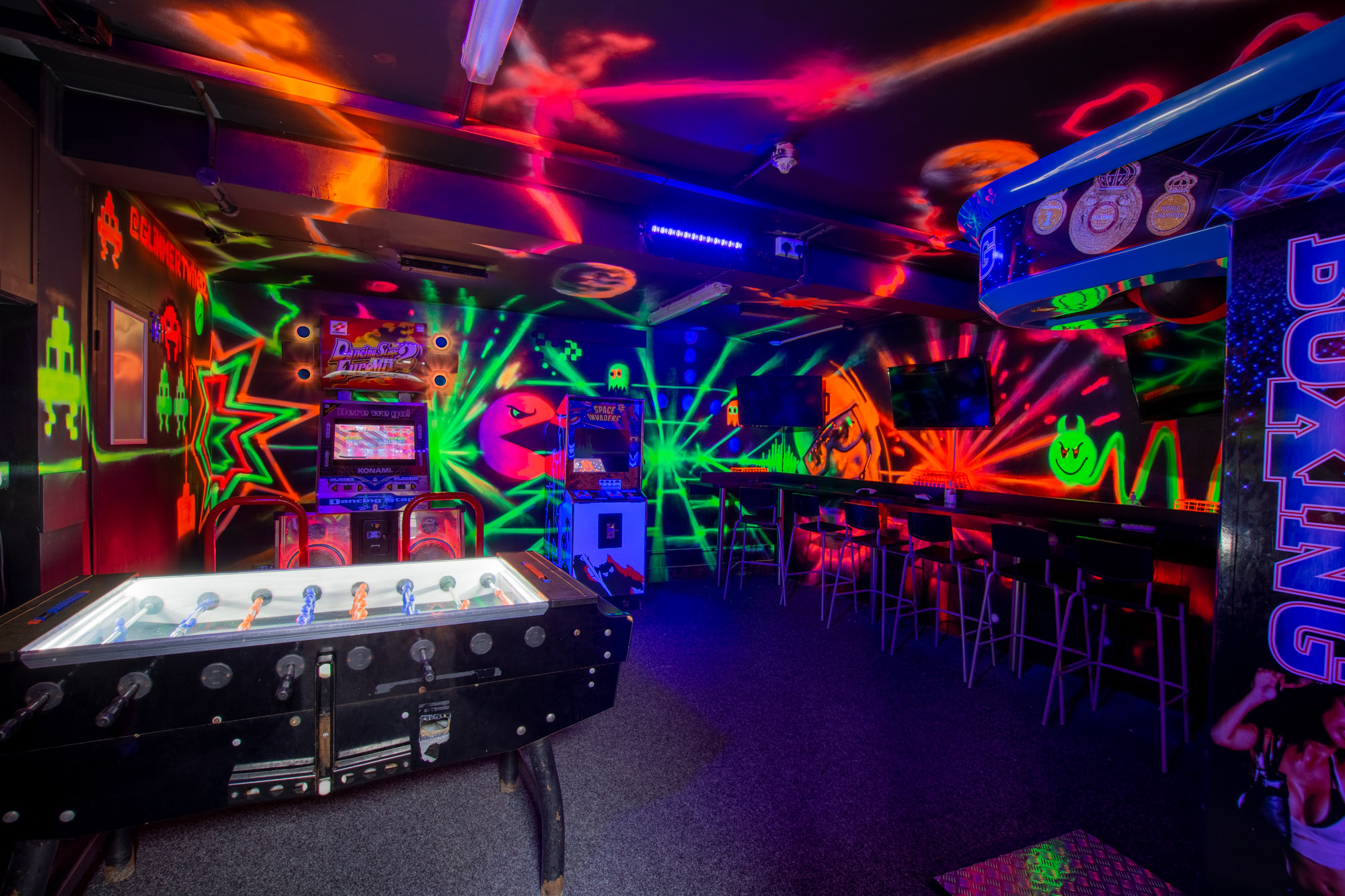 Vibrant neon-lit venue for corporate events with arcade games and foosball.