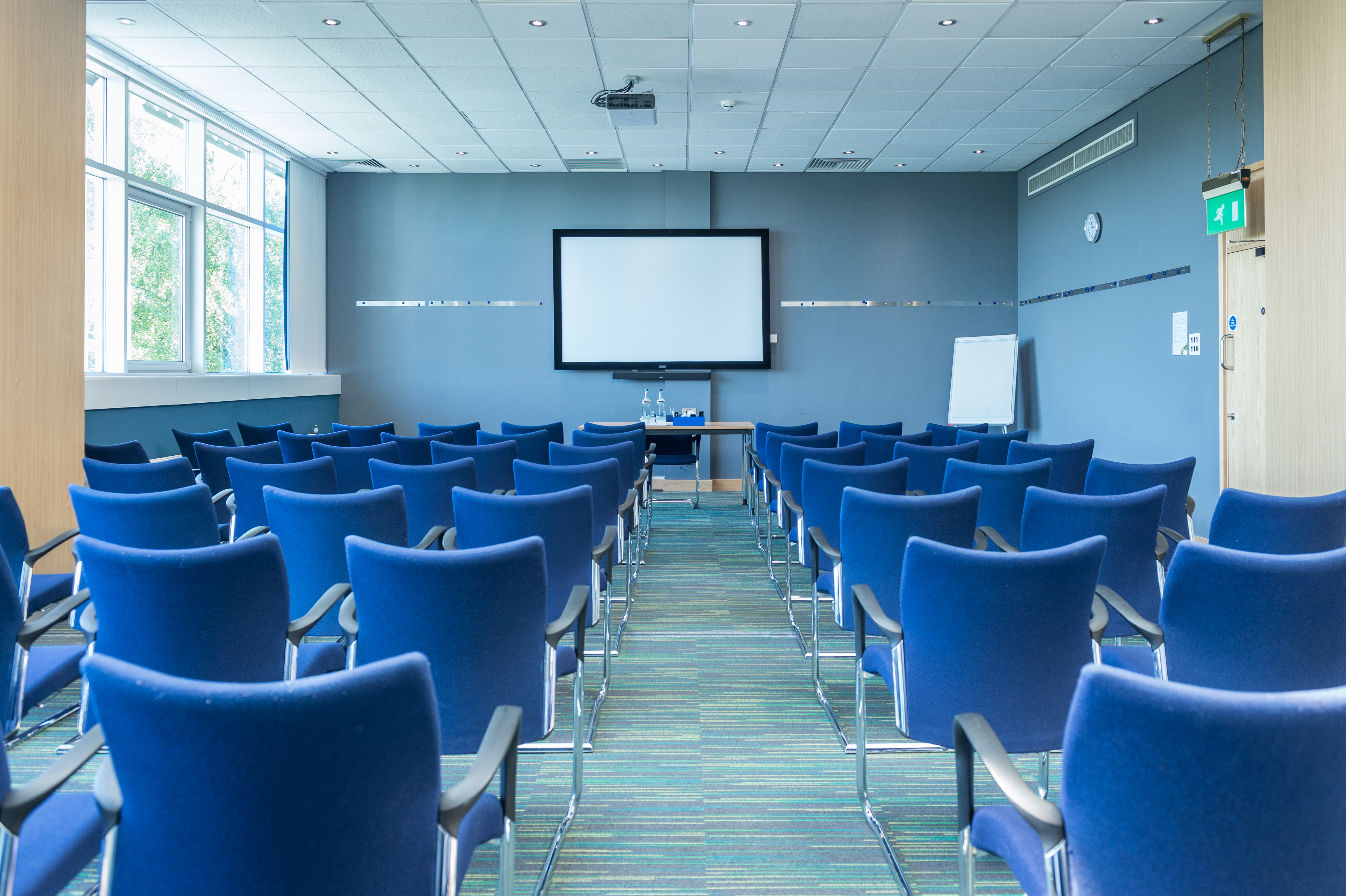 Meeting room with blue chairs and screen, perfect for corporate workshops and presentations.