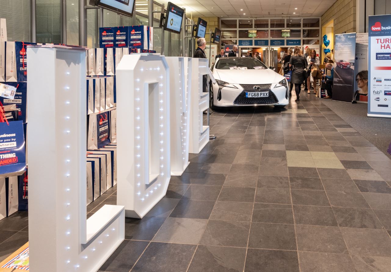 Event space at Holywell Park with illuminated "LOV" signage and sleek car for networking.