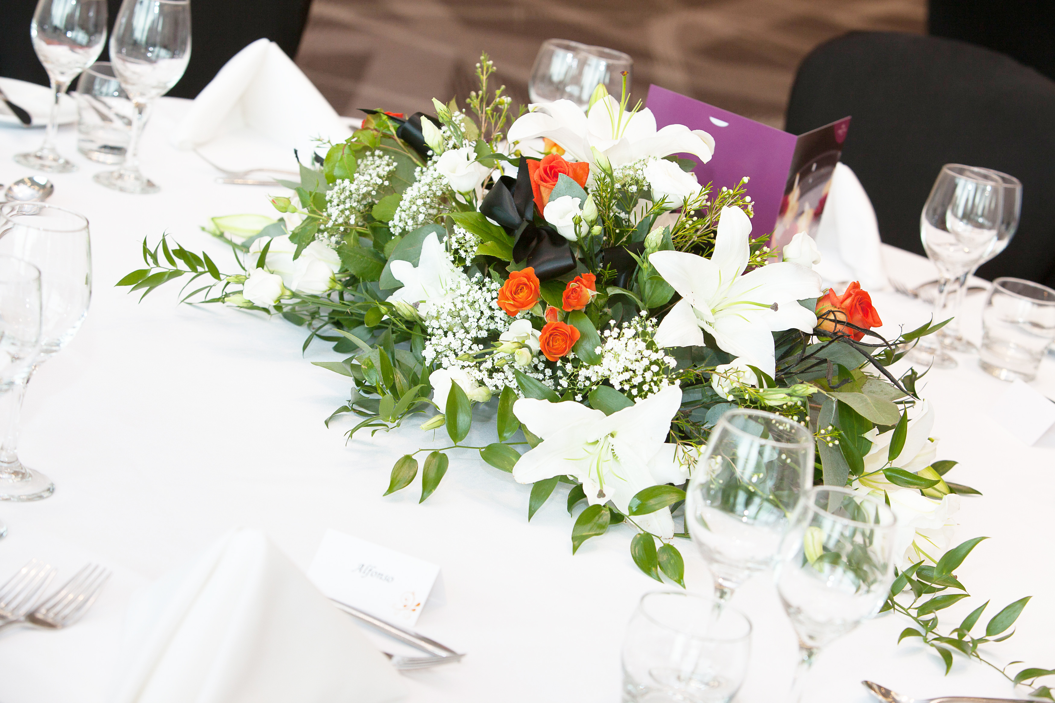 Elegant floral centerpiece with white lilies and orange roses at Crowne Plaza Marlow event.
